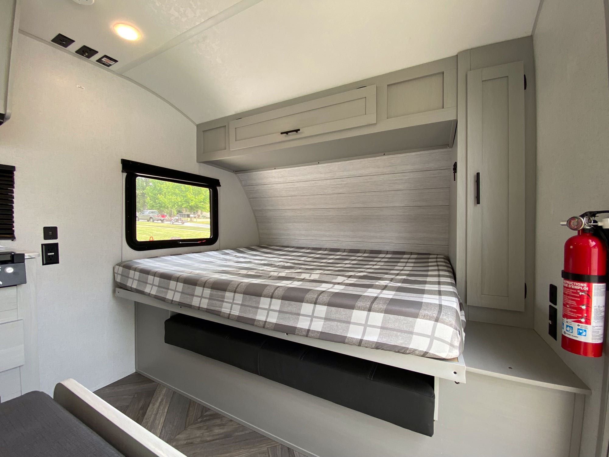 Step into this cozy RV rental bedroom. Features a comfortable plaid bed, overhead cabinets, outlets, and a fire extinguisher.. Forest River Salem 2021