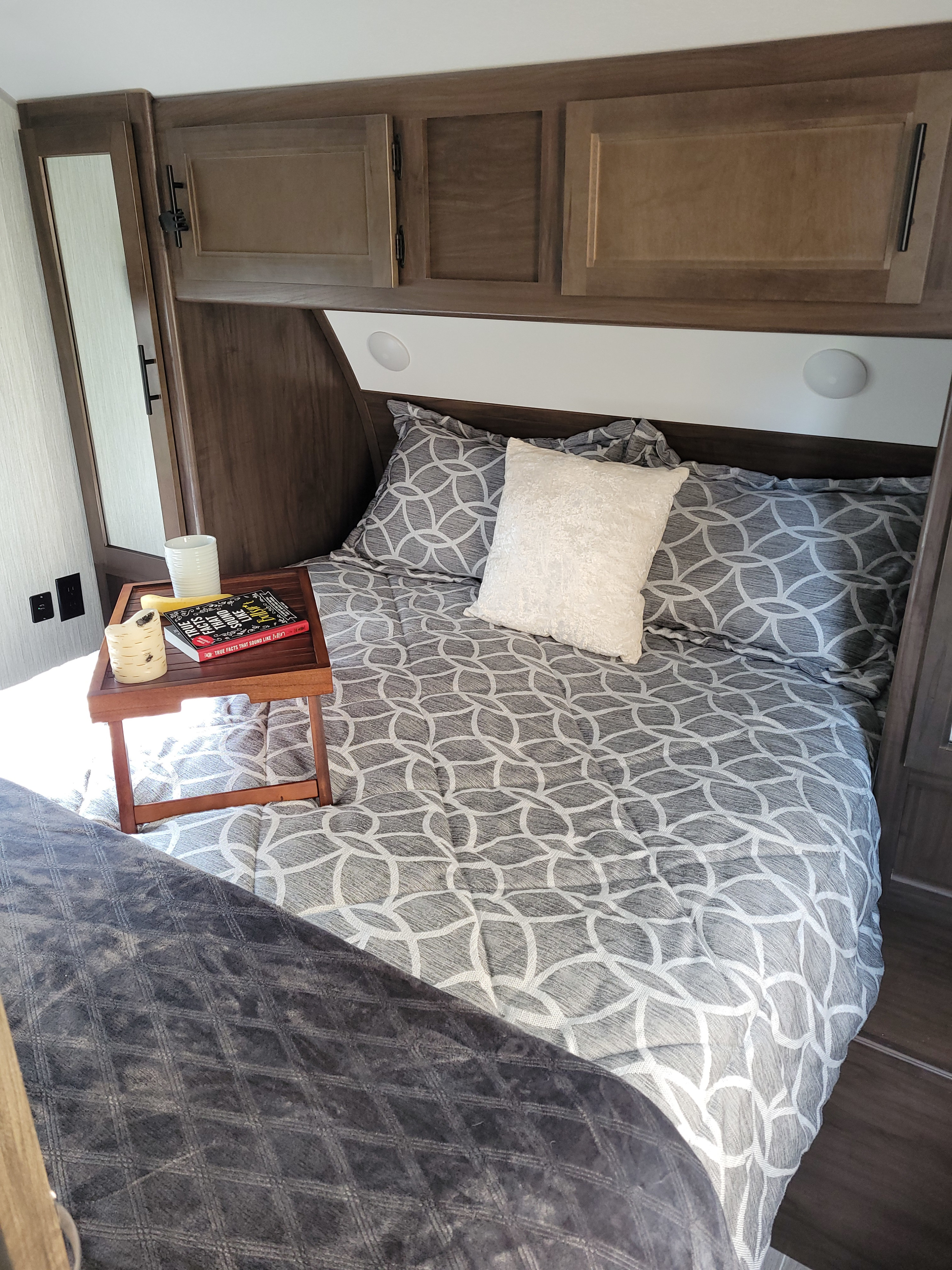 Interior view of a comfortable RV rental bedroom featuring geometric patterned bedding, wood cabinets, and a bedside tray.. Forest River Other 2021