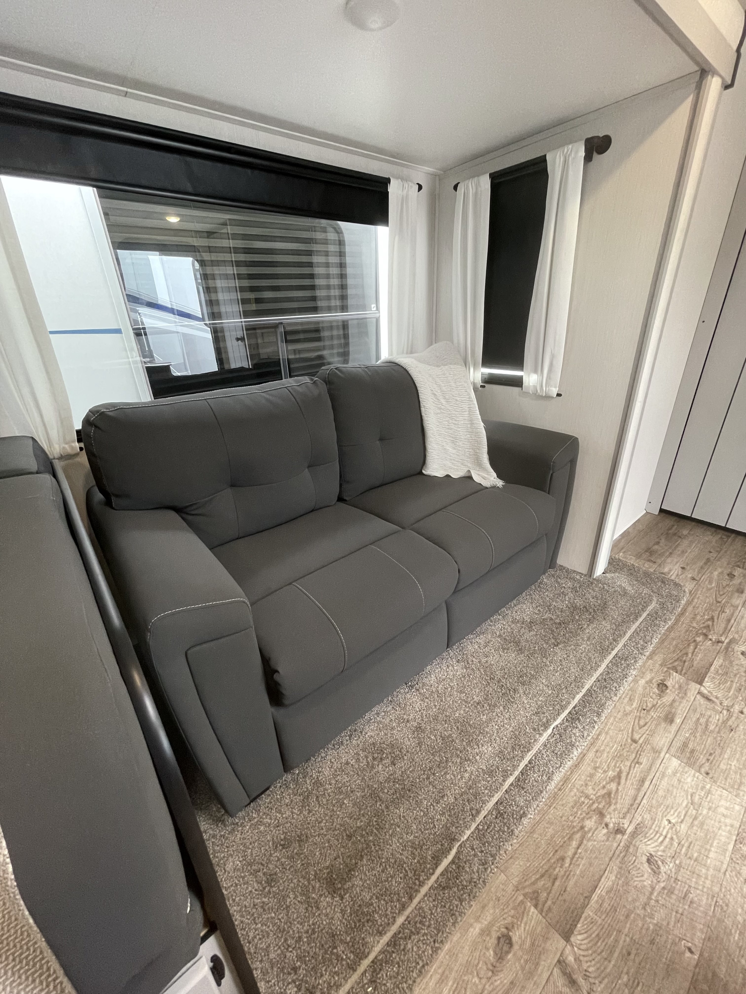 Spacious RV rental interior: A dark grey, tufted sofa with white throw, large windows, and sheer white curtains create a bright living space.. Forest River Vibe 2021