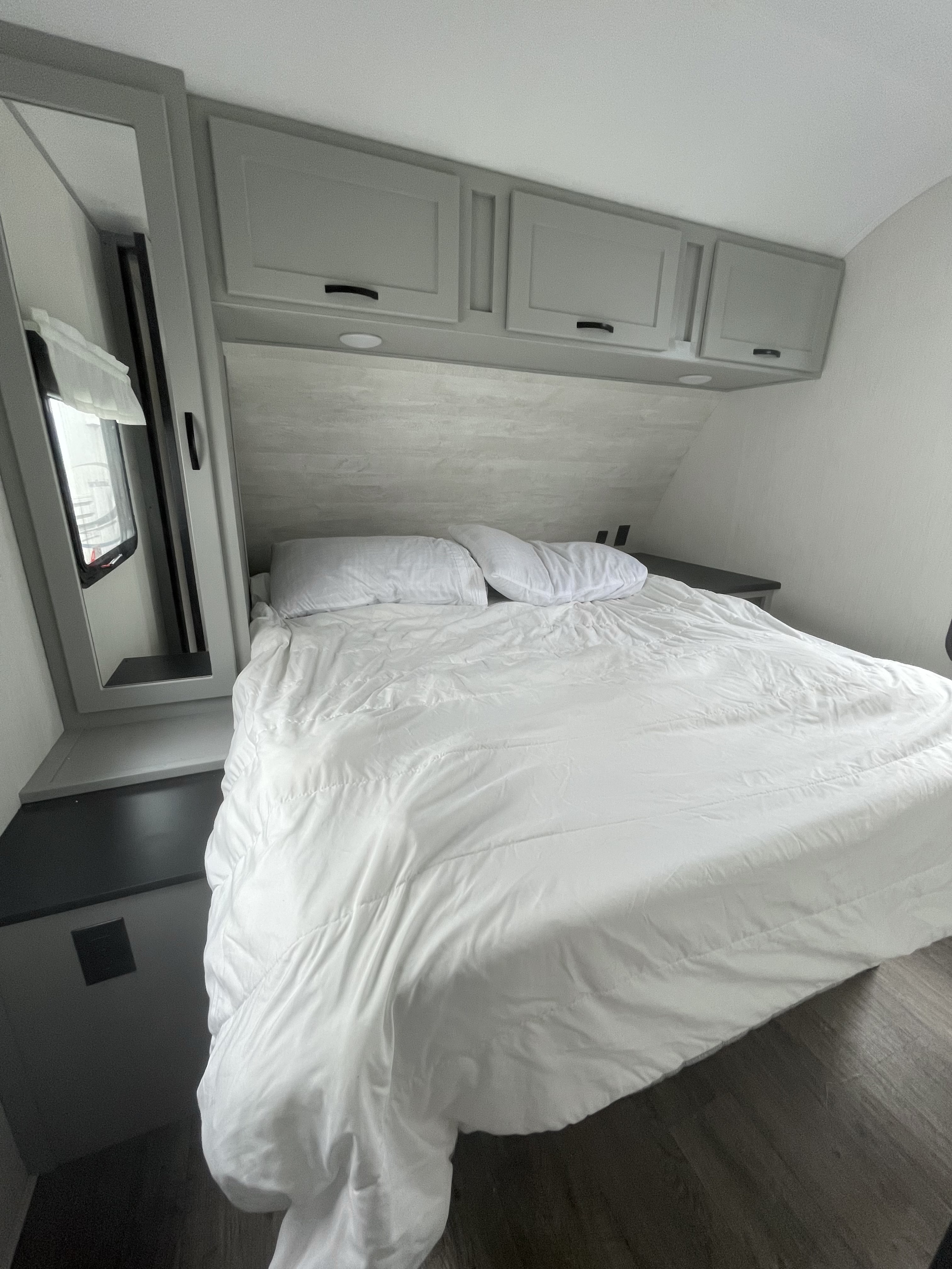 Cozy RV rental bedroom featuring a large bed with white linens, grey cabinetry, and a mirrored side panel for added space.. Forest River Vibe 2021