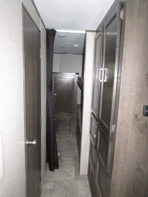 This RV rental interior shows a narrow hallway with a door, dark privacy curtain for a bunk area, and storage cabinets.. Jayco Jay Flight SLX 2021