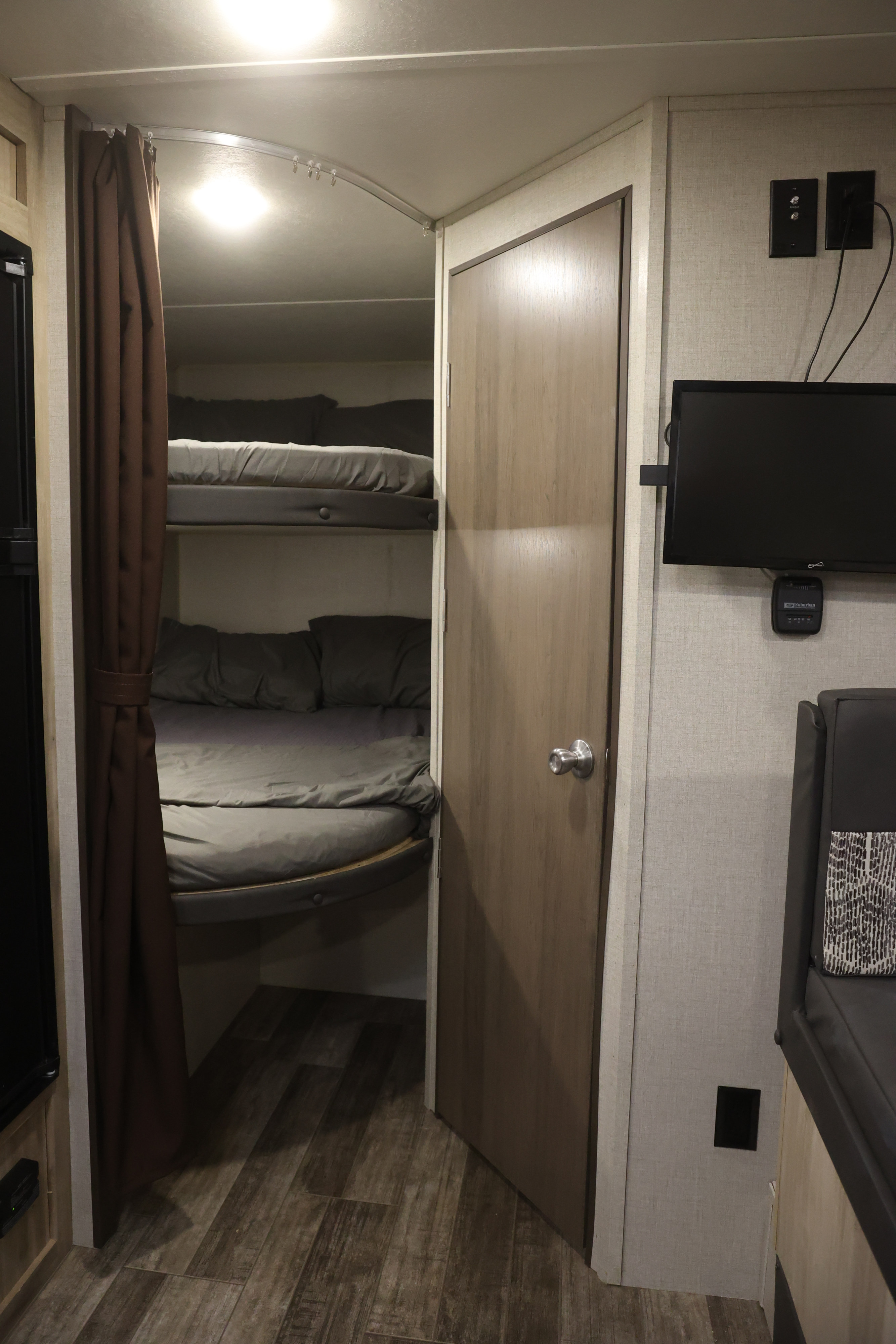 Cozy rv rental interior featuring a bunk bed area with privacy curtains, a door, and a wall-mounted TV, showcasing compact travel living.. Coachmen Catalina 2021