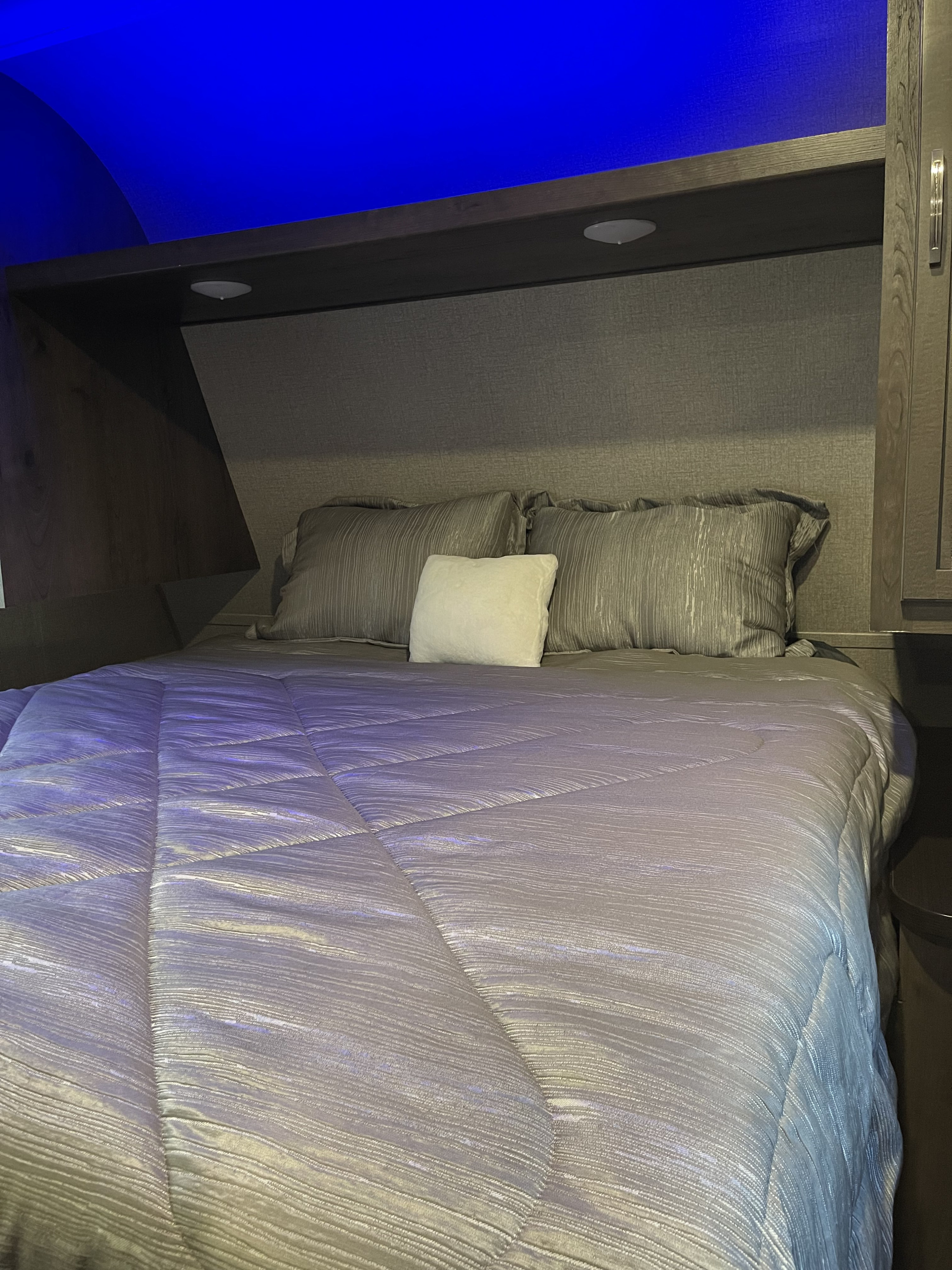 Cozy RV rental bedroom featuring a made bed with gray bedding, blue mood lighting, and built-in storage.. Jayco Jay Flight 2020