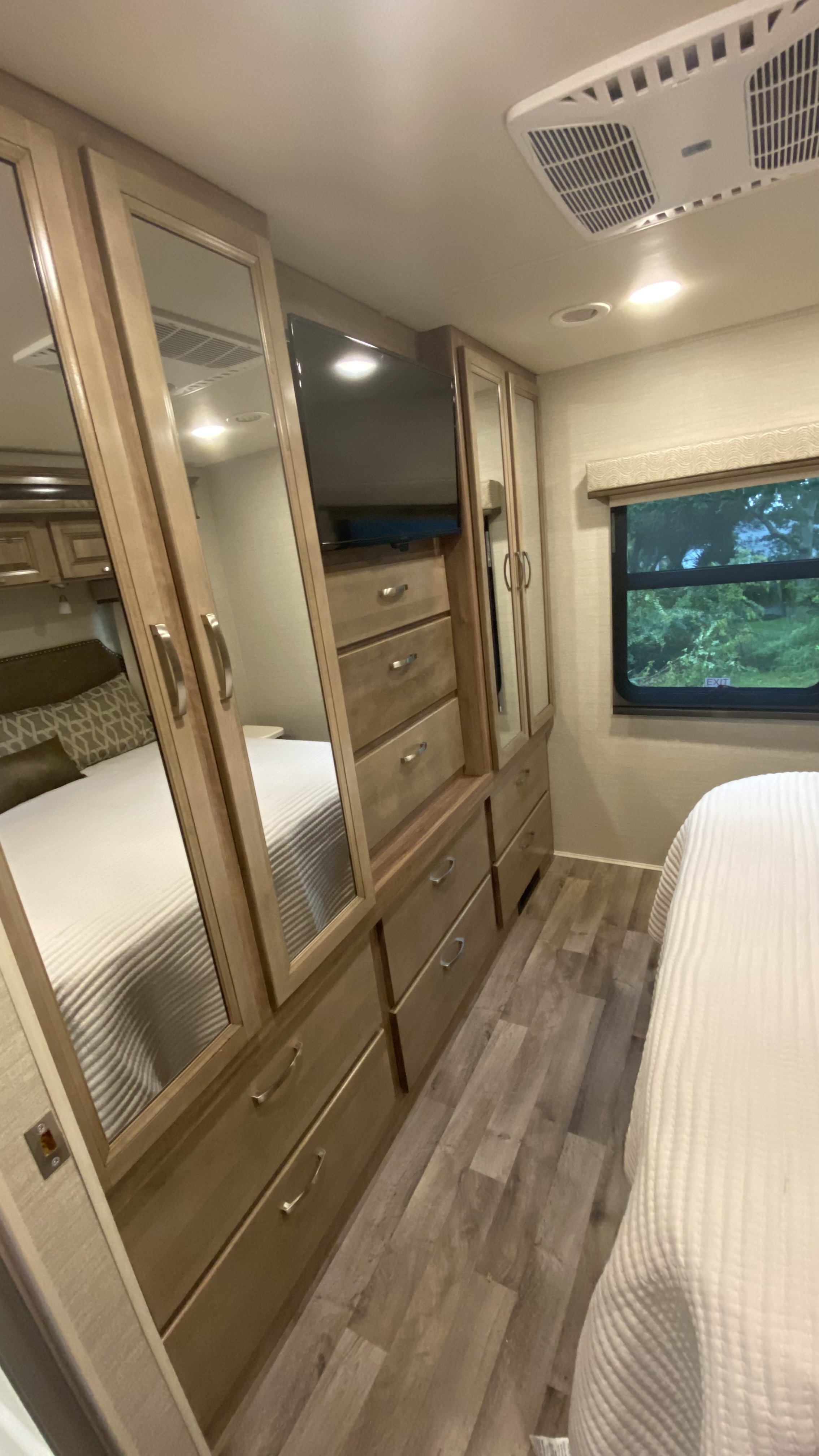 Cozy RV rental bedroom featuring mirrored wardrobe, dresser with TV, comfortable bed, and scenic window view.. Jayco Precept 2019