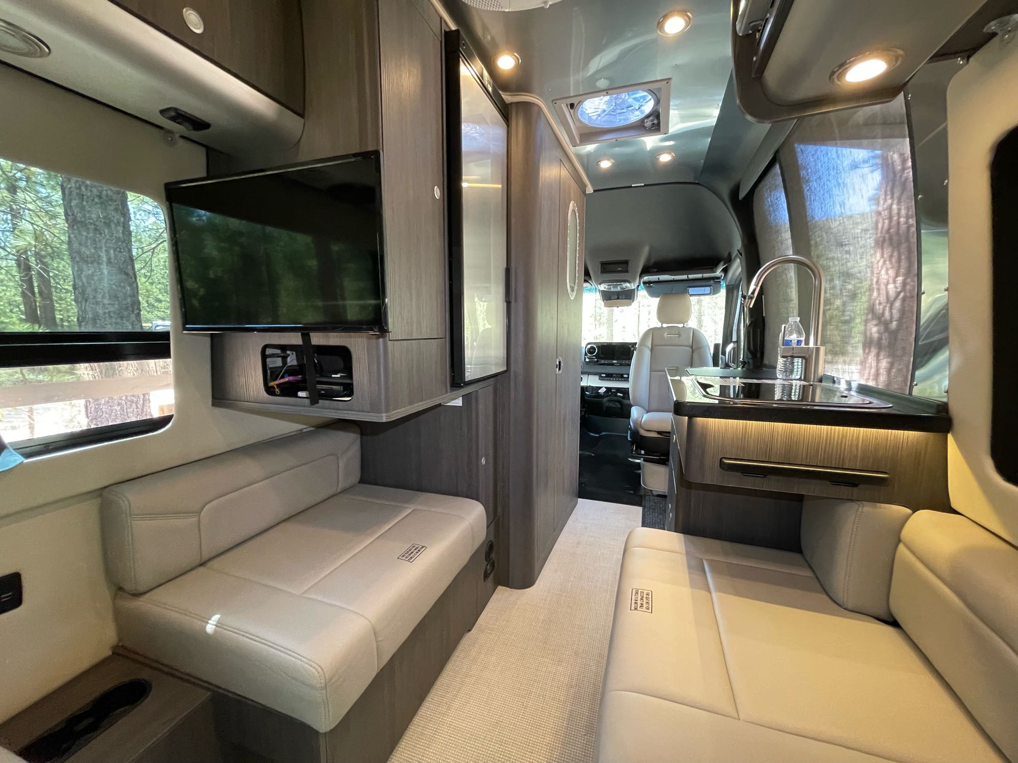 Spacious RV rental interior with plush seating, a TV, and a functional kitchen area.. Airstream Interstate 2021