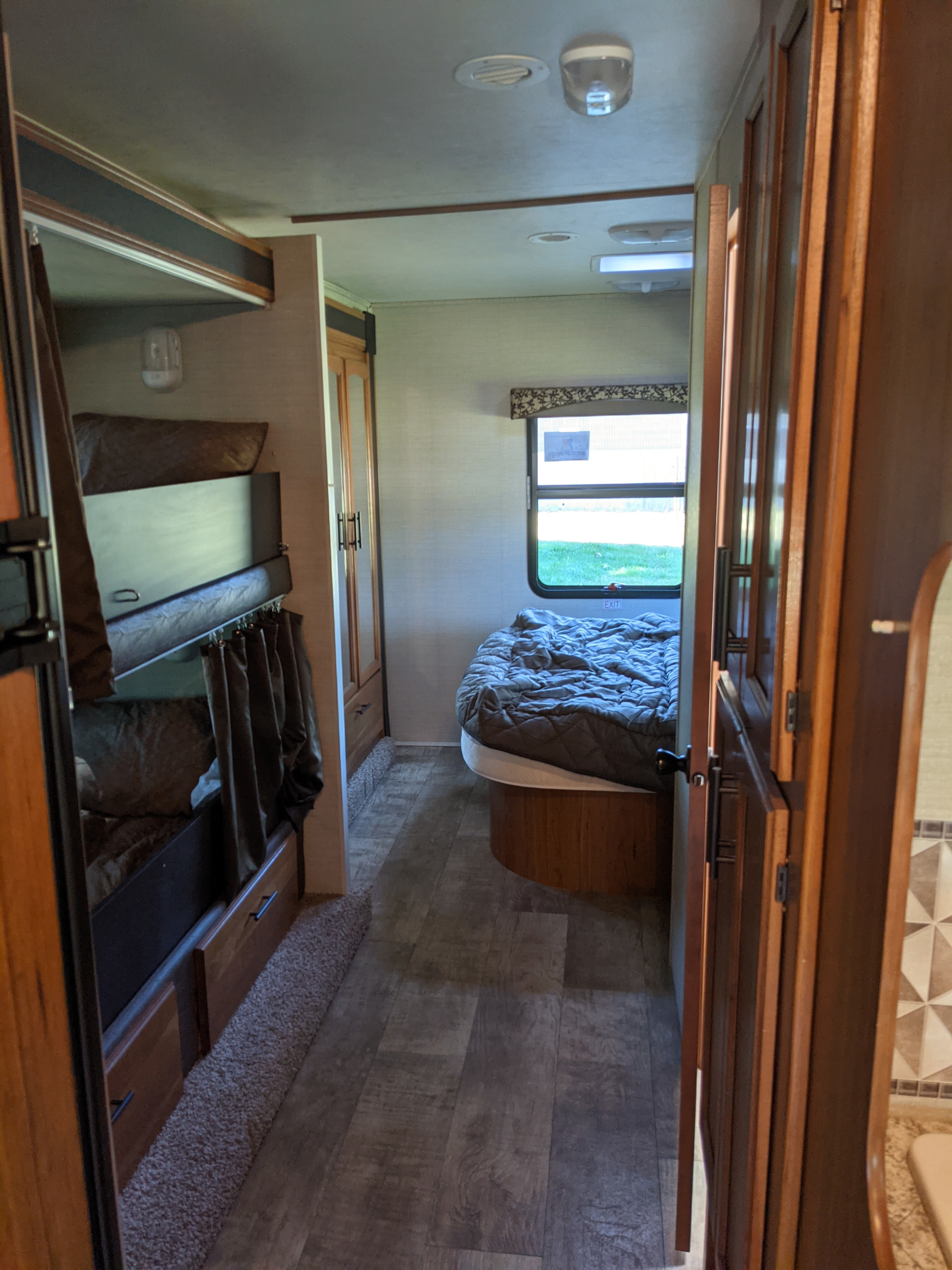 RV rental interior: A hallway leads past bunk beds on the left to a private bedroom with a window, featuring wood-look flooring.. Jayco Redhawk 2017