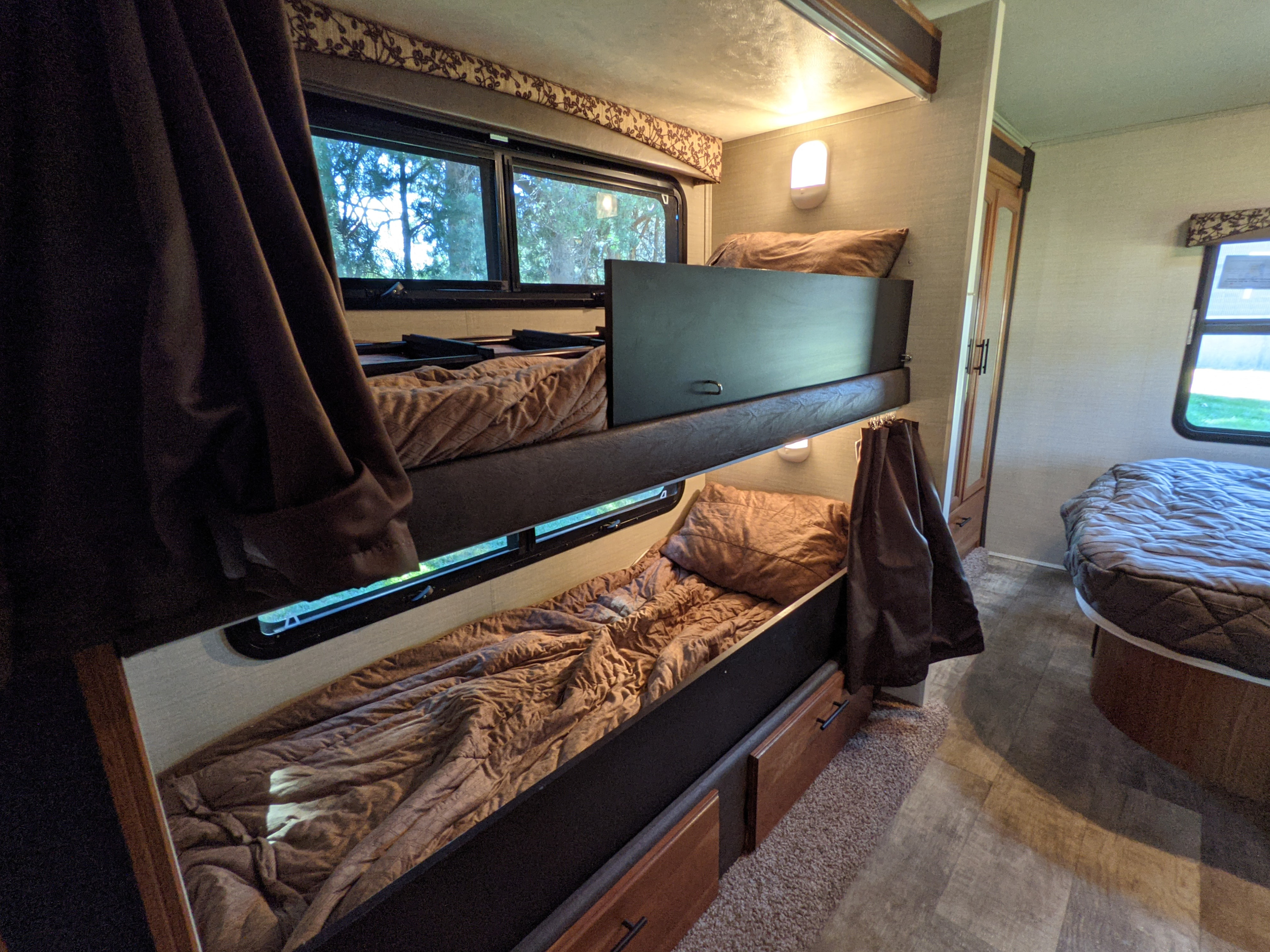 An RV rental bedroom features two cozy bunk beds with windows, a separate main bed, and built-in storage.. Jayco Redhawk 2017