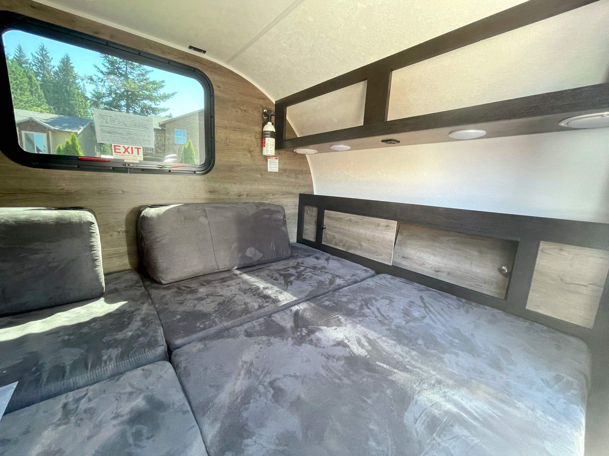 Cozy RV rental interior featuring a versatile grey sofa/bed, window with an outdoor view, and convenient overhead storage.. Braxton Creek Bushwhacker 2021