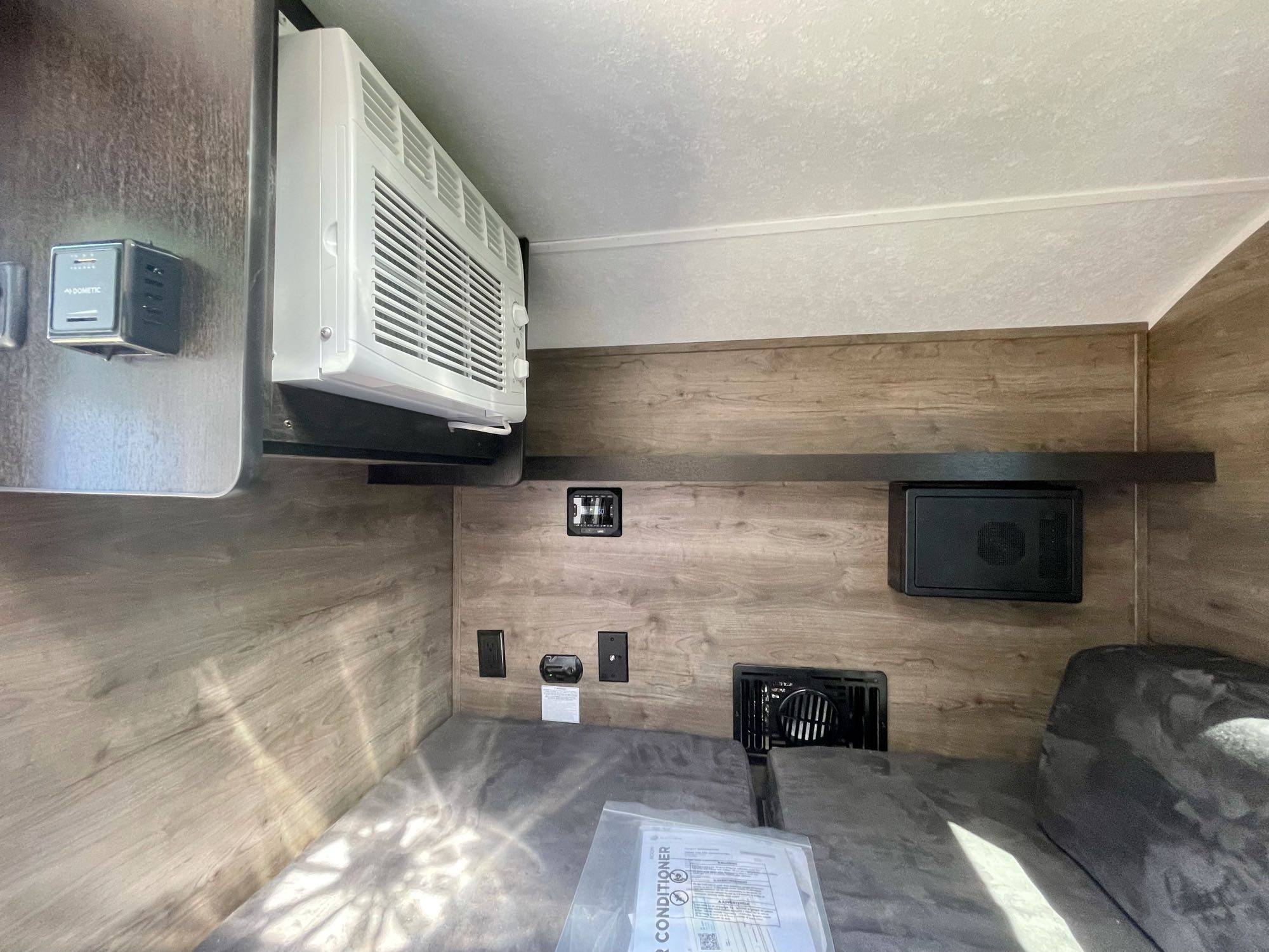 RV rental interior showing AC unit, Dometic controls, outlets, and a compact sleeping area with wood-paneled walls.. Braxton Creek Bushwhacker 2021
