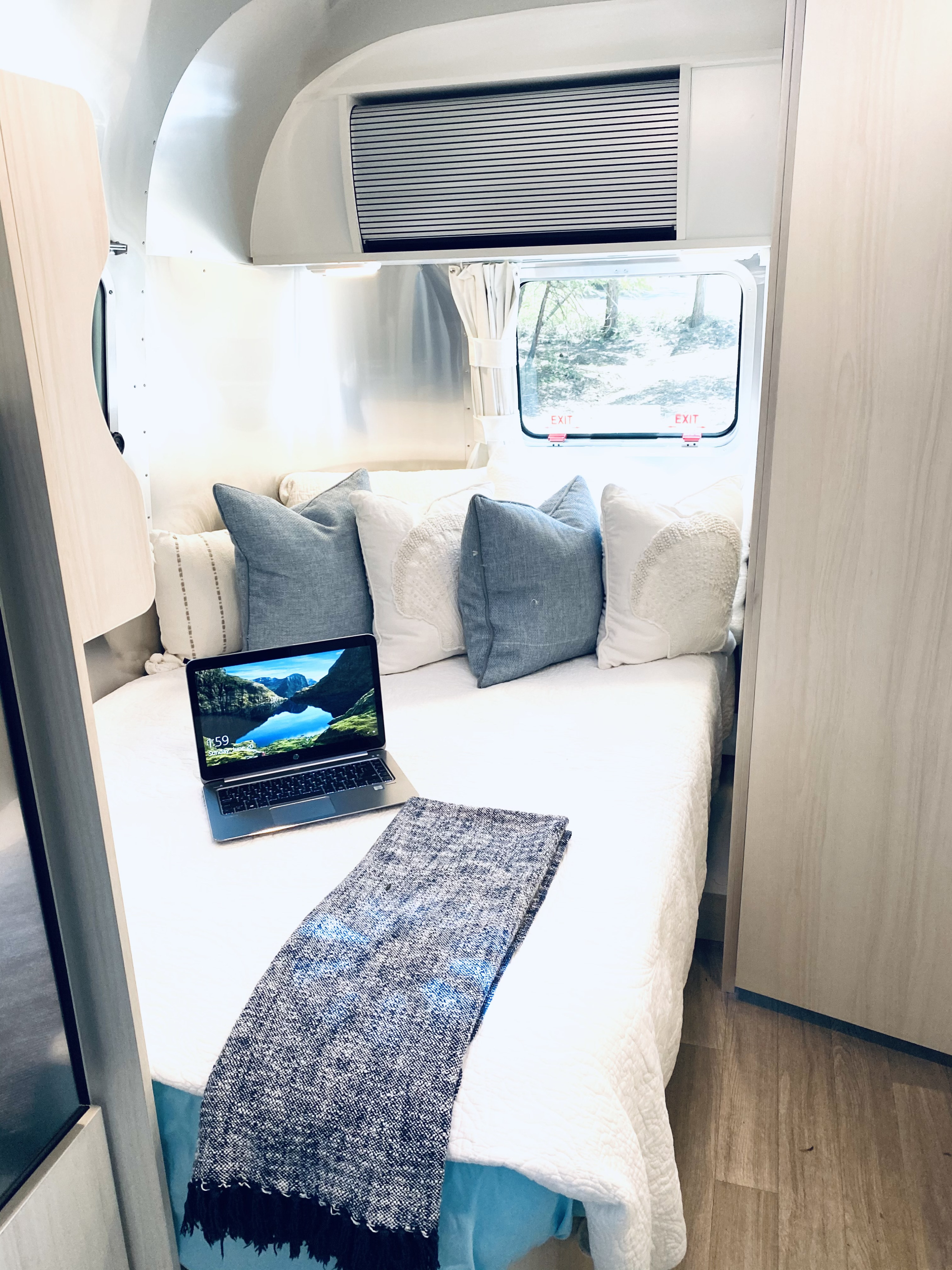 Modern RV rental interior featuring a cozy bed with decorative pillows, a laptop, and an outdoor window view.. Airstream Bambi 2022