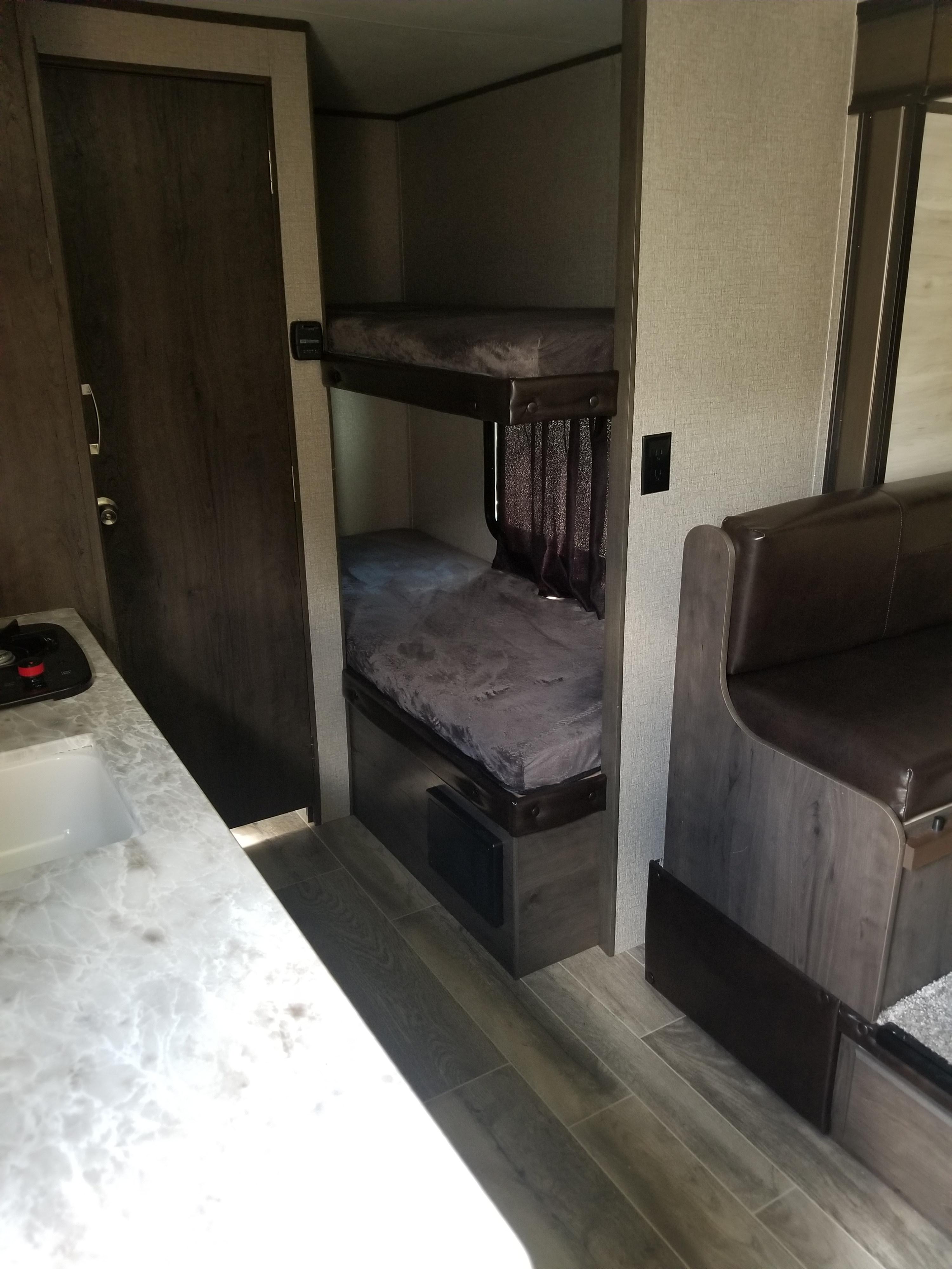 This RV rental interior features a kitchen counter, a dark wood door, bunk beds, and a dinette area.. Jayco Jay Flight 2021