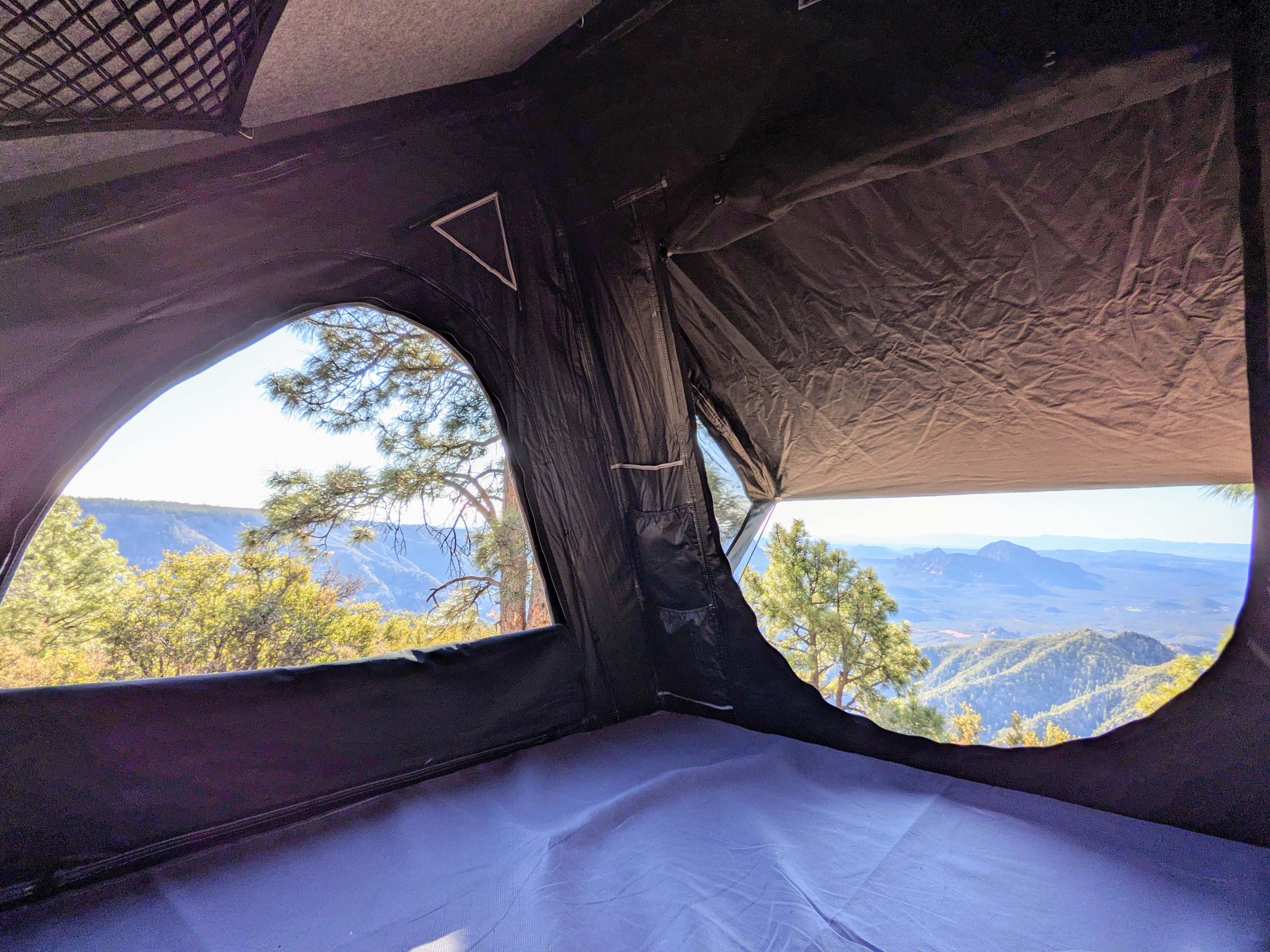 Interior of an RV rental rooftop tent, showcasing expansive mountain views through large arched windows. Ideal for nature lovers.. Jeep Wrangler 2020