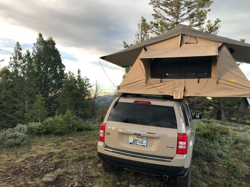 Jeep Patriot with a rooftop tent deployed in a scenic, forested mountain setting. A unique off-grid alternative to traditional RV rental for nature lovers.. Jeep Patriot 2016