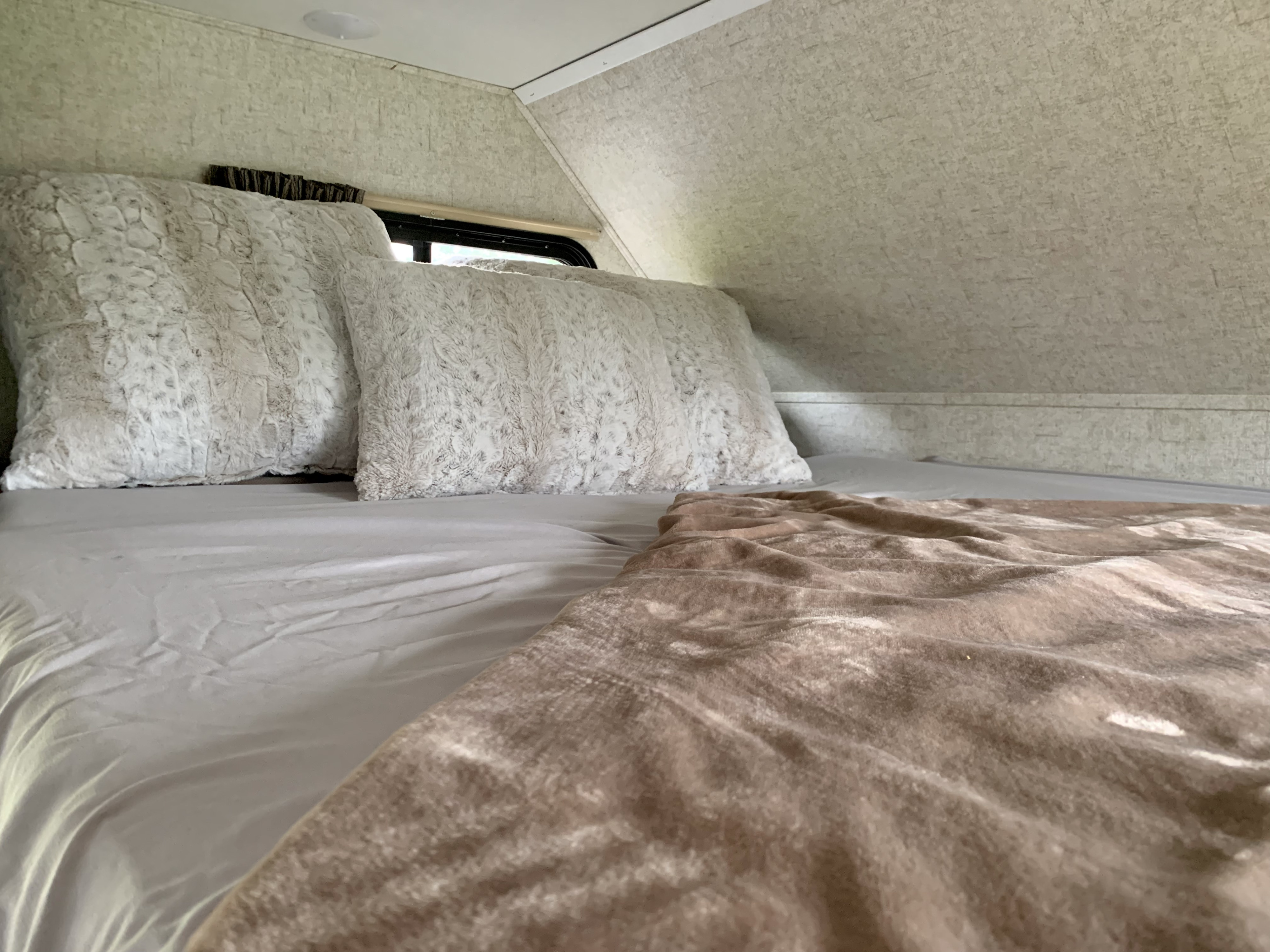 Cozy RV rental bedroom with soft, light-colored bedding and fluffy pillows, offering a comfortable space for travel.. Forest River Sunseeker 2018