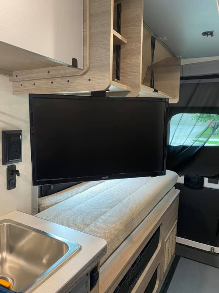 View inside an rv rental, featuring a mounted TV under wooden cabinets, a small sink, and a cushioned bed area. Compact and functional.. Winnebago Other 2022