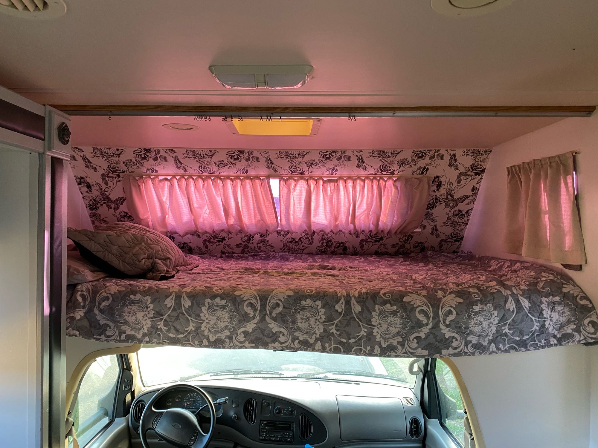RV rental's cozy cab-over bunk, featuring a patterned bed, pink lighting, and vehicle dashboard below.. Holiday Rambler Atlantis 2002