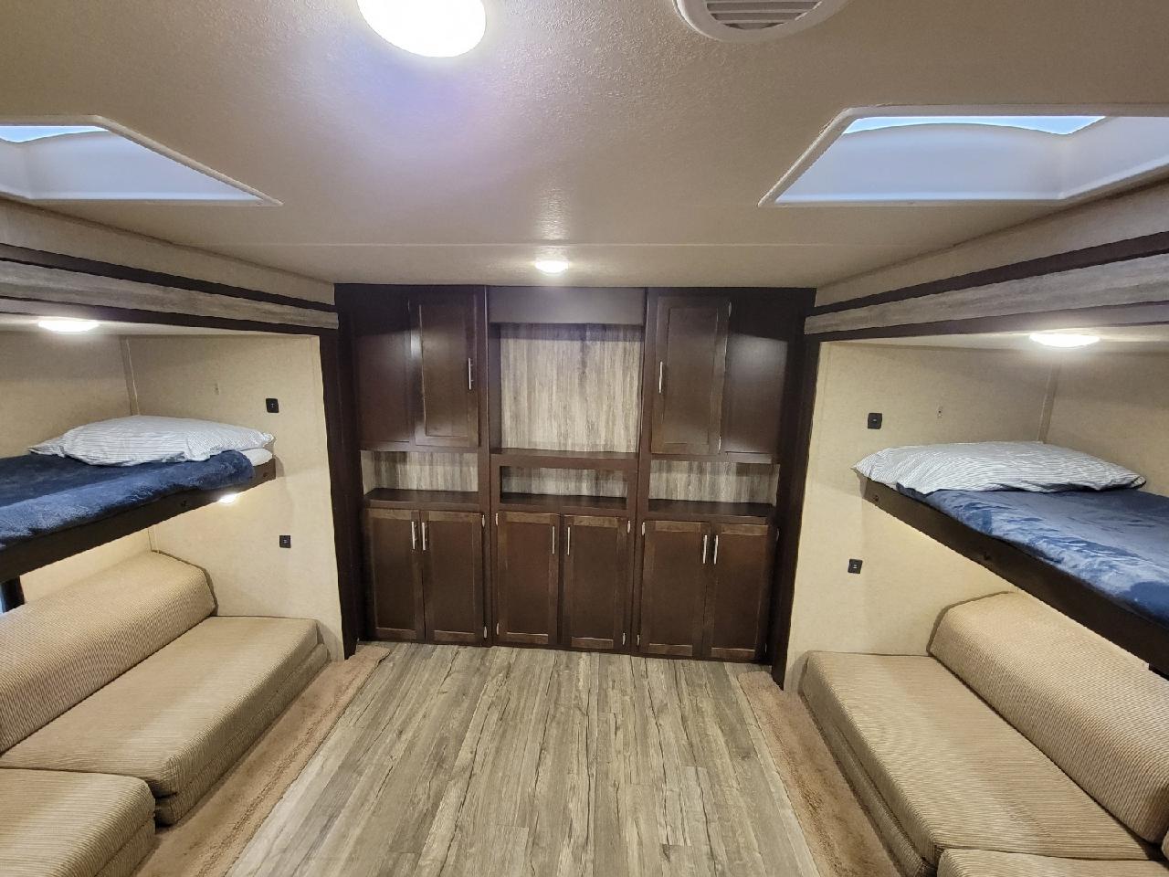 This RV rental interior features a cozy bunkhouse with beds, convertible sofas, and central storage, perfect for group trips.. Forest River Cherokee 2017