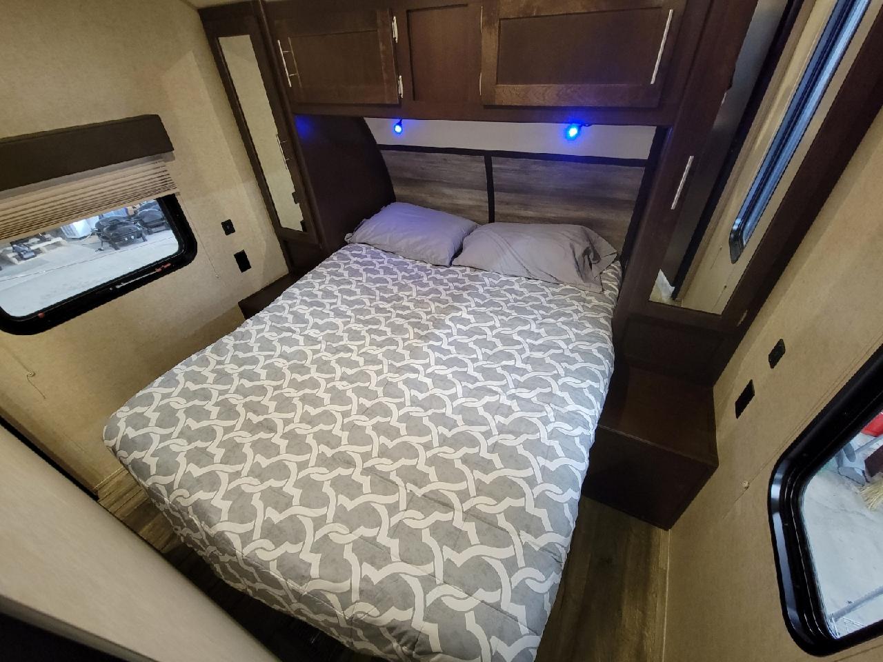 Cozy RV rental bedroom with patterned bed, overhead cabinets, and blue lighting. Compact travel trailer space for rent.. Forest River Cherokee 2017