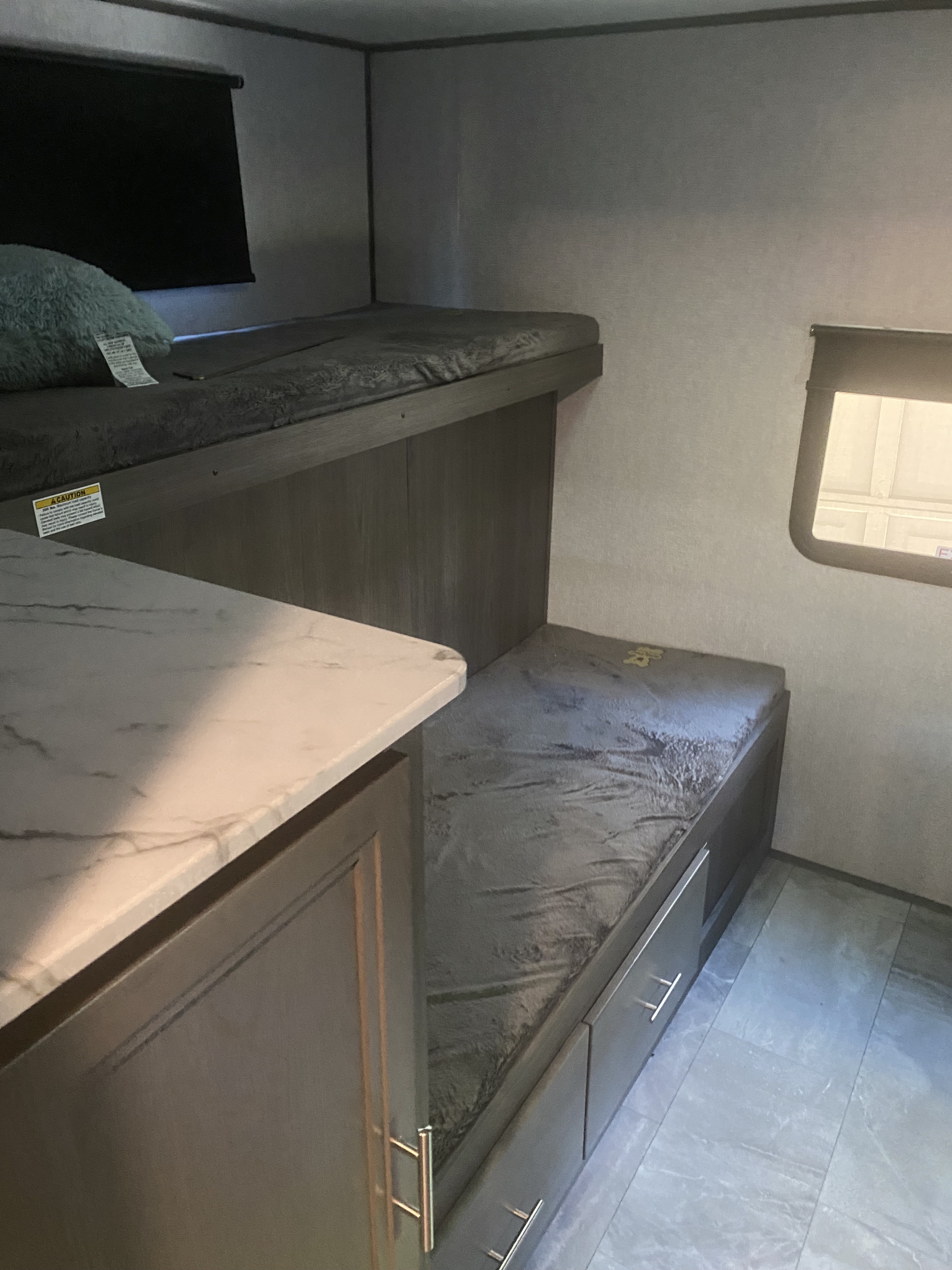 This RV rental interior features two bunk beds with a pillow, under-bunk storage drawers, and a window, creating a cozy sleeping area.. Dutchmen Kodiak 2021