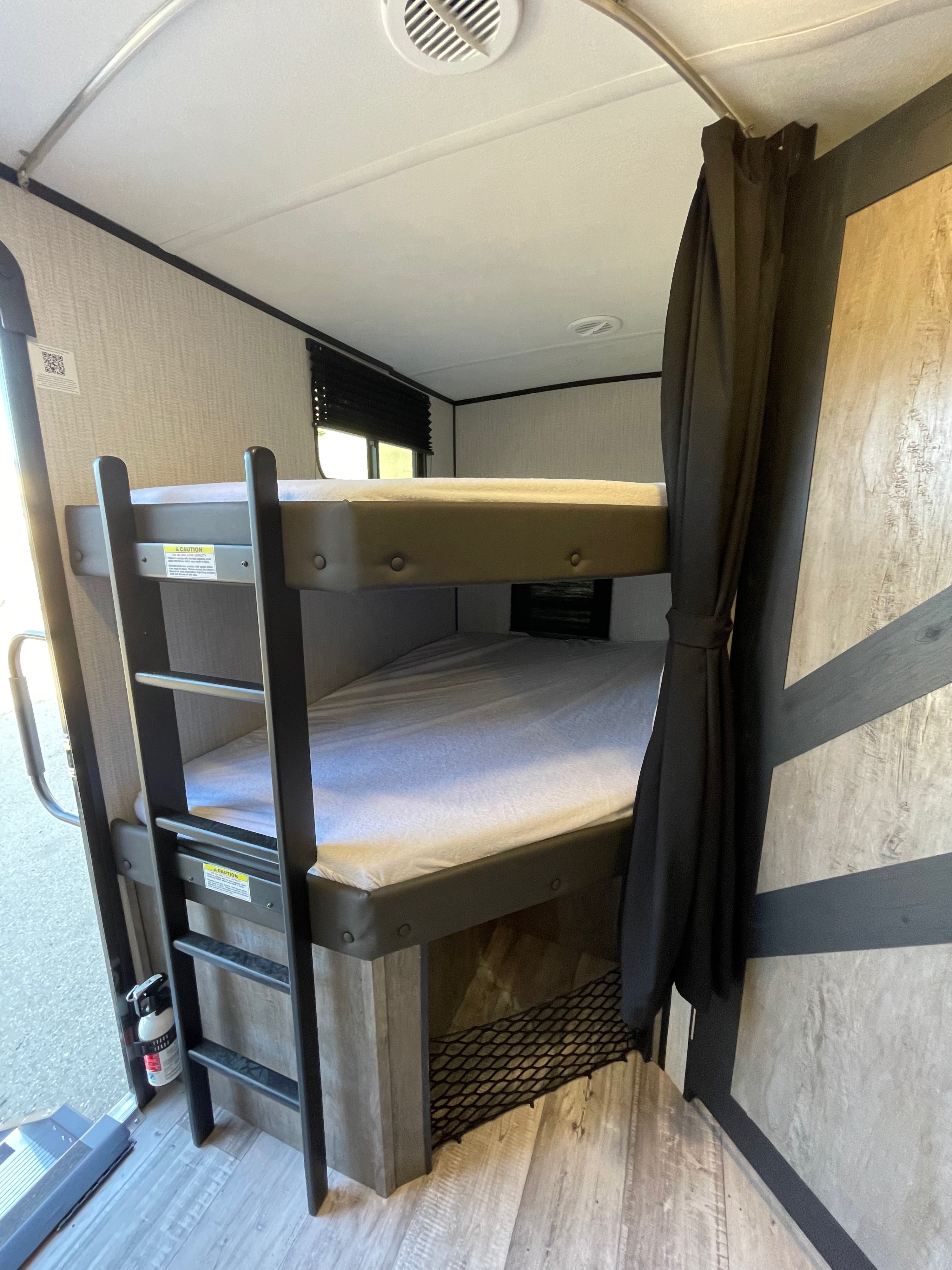 This RV rental interior features practical bunk beds, a ladder, and a visible fire extinguisher for safe and cozy travel.. Heartland North Trail 2021