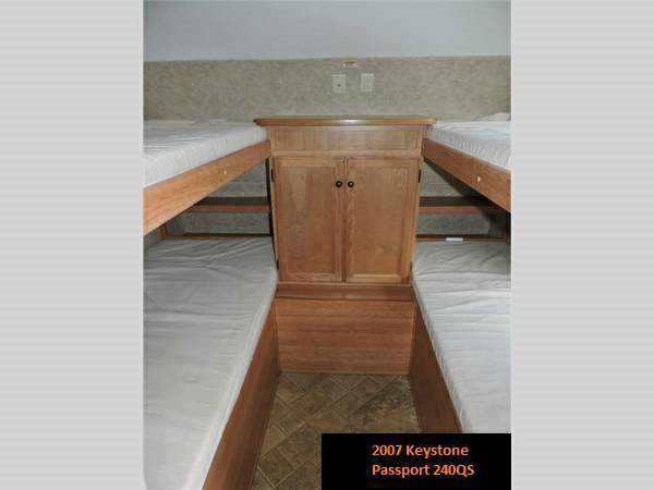 RV rental sleeping area featuring two sets of bunk beds and a central storage cabinet. Ideal for family adventures.. Keystone RV Passport 2007