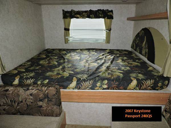 RV rental interior featuring a large bed with tropical patterned bedding, window, and storage shelf.. Keystone RV Passport 2007