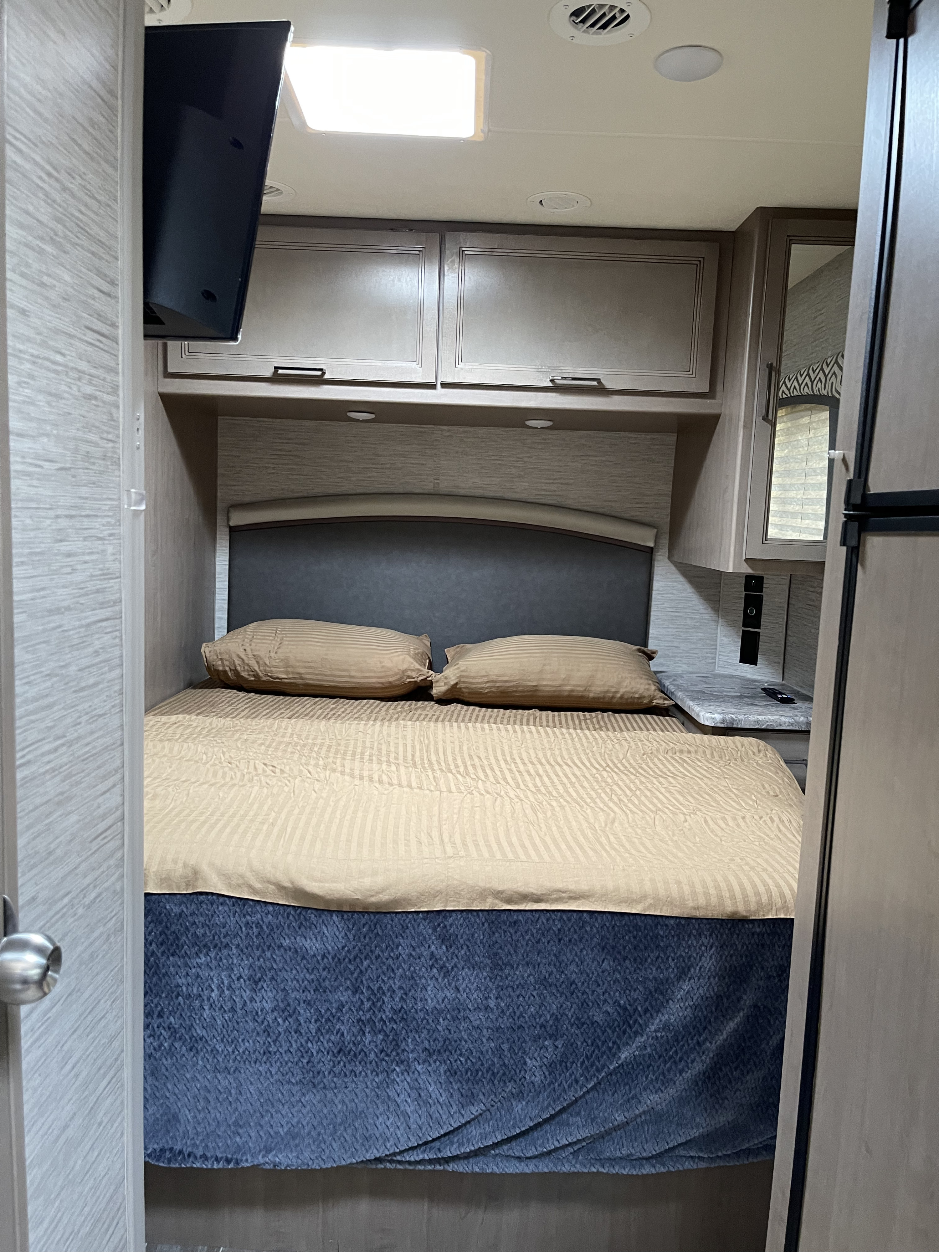 Inside an RV rental bedroom featuring a comfortable bed, overhead storage, TV, and small nightstand.. Thor Motor Coach Chateau 2021