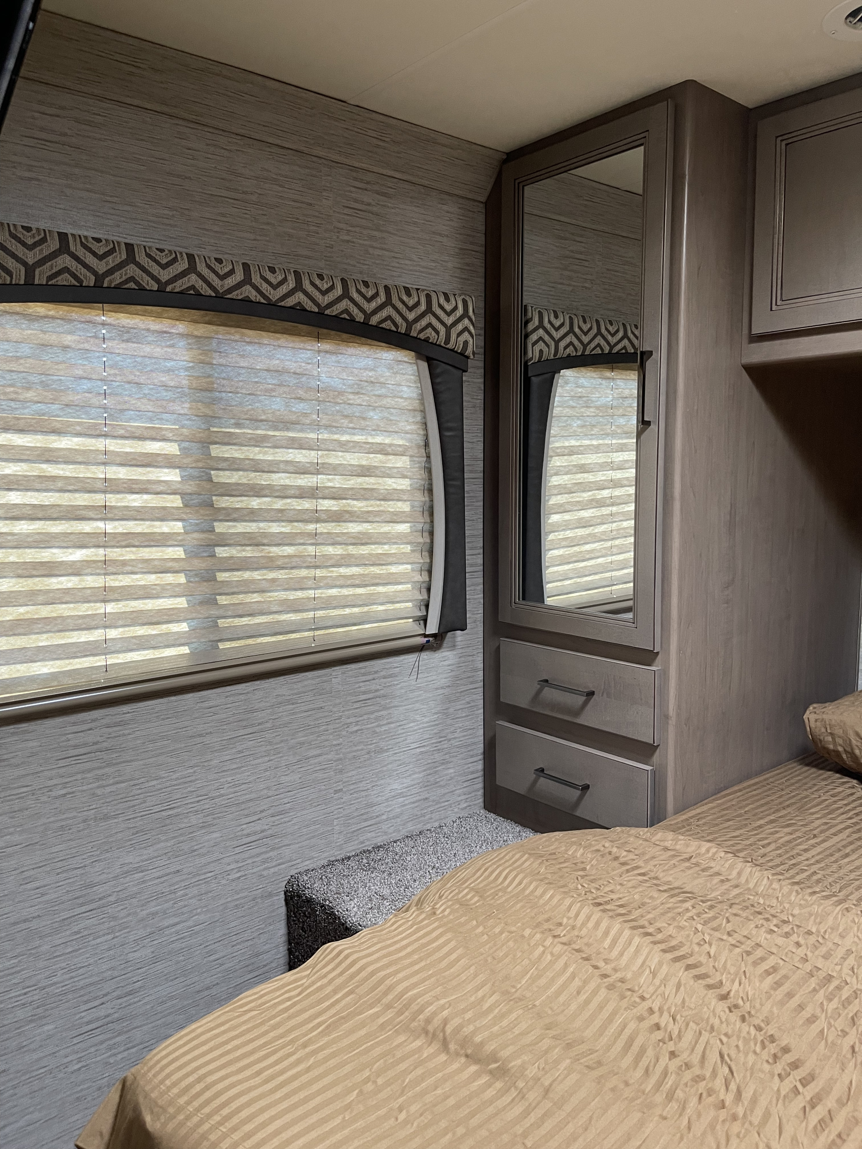 Comfortable RV rental bedroom with striped bedding, mirrored wardrobe, and window blinds. Ideal for road trips.. Thor Motor Coach Chateau 2021