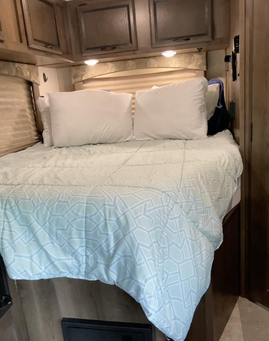 RV rental bedroom: cozy bed with light blue patterned comforter, white pillows, and overhead storage cabinets.. ford Other 2019