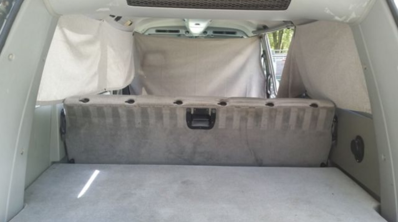 RV rental interior: A converted vehicle sleeping area with a gray bed base, seat back, and privacy curtains.. Volkswagen Vanagon 1987