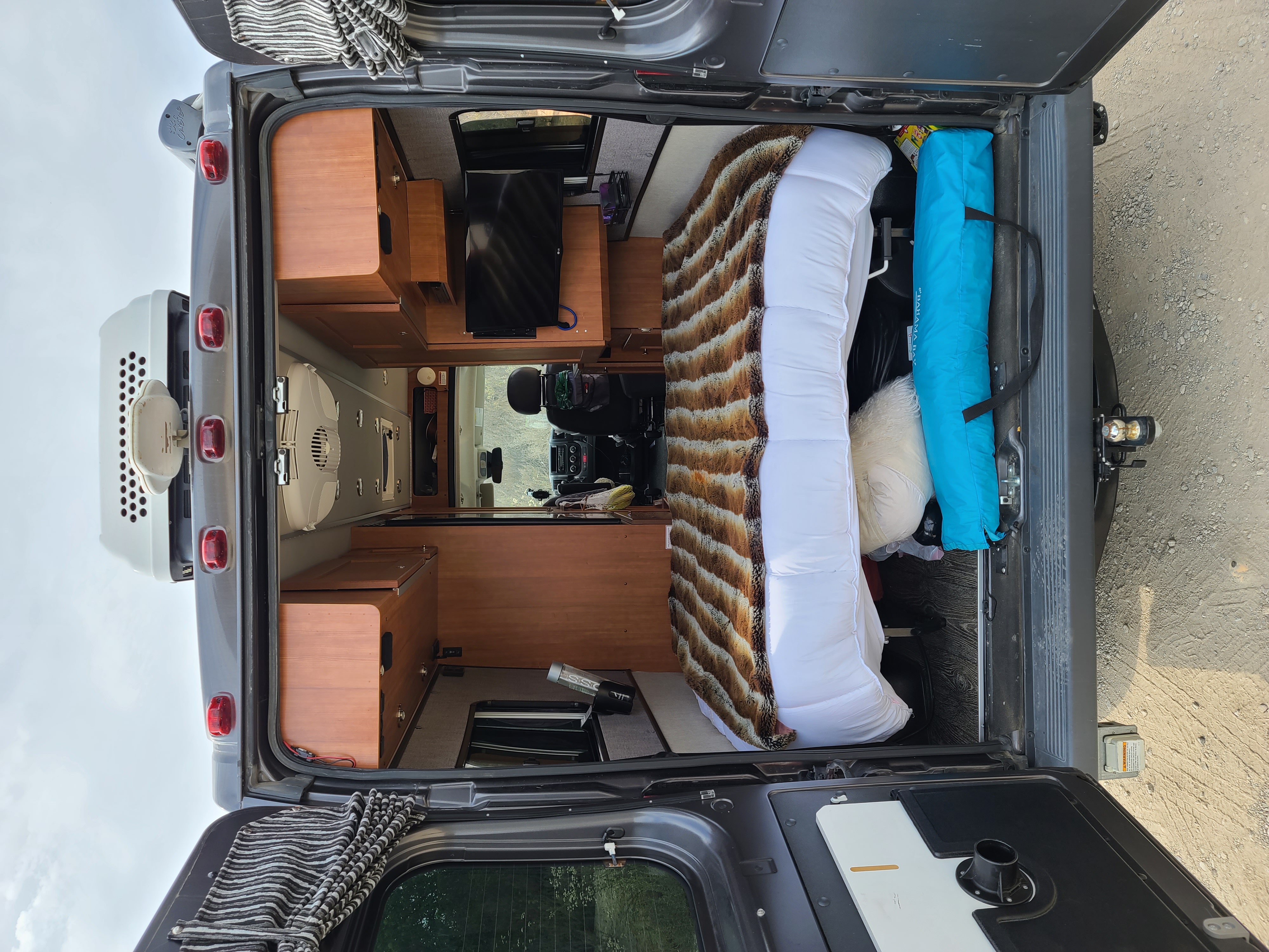 Inside a comfortable rv rental camper van, showing a full bed, TV, and wood cabinetry, ready for your travel adventures.. Roadtrek Roadtrek Class B 2018