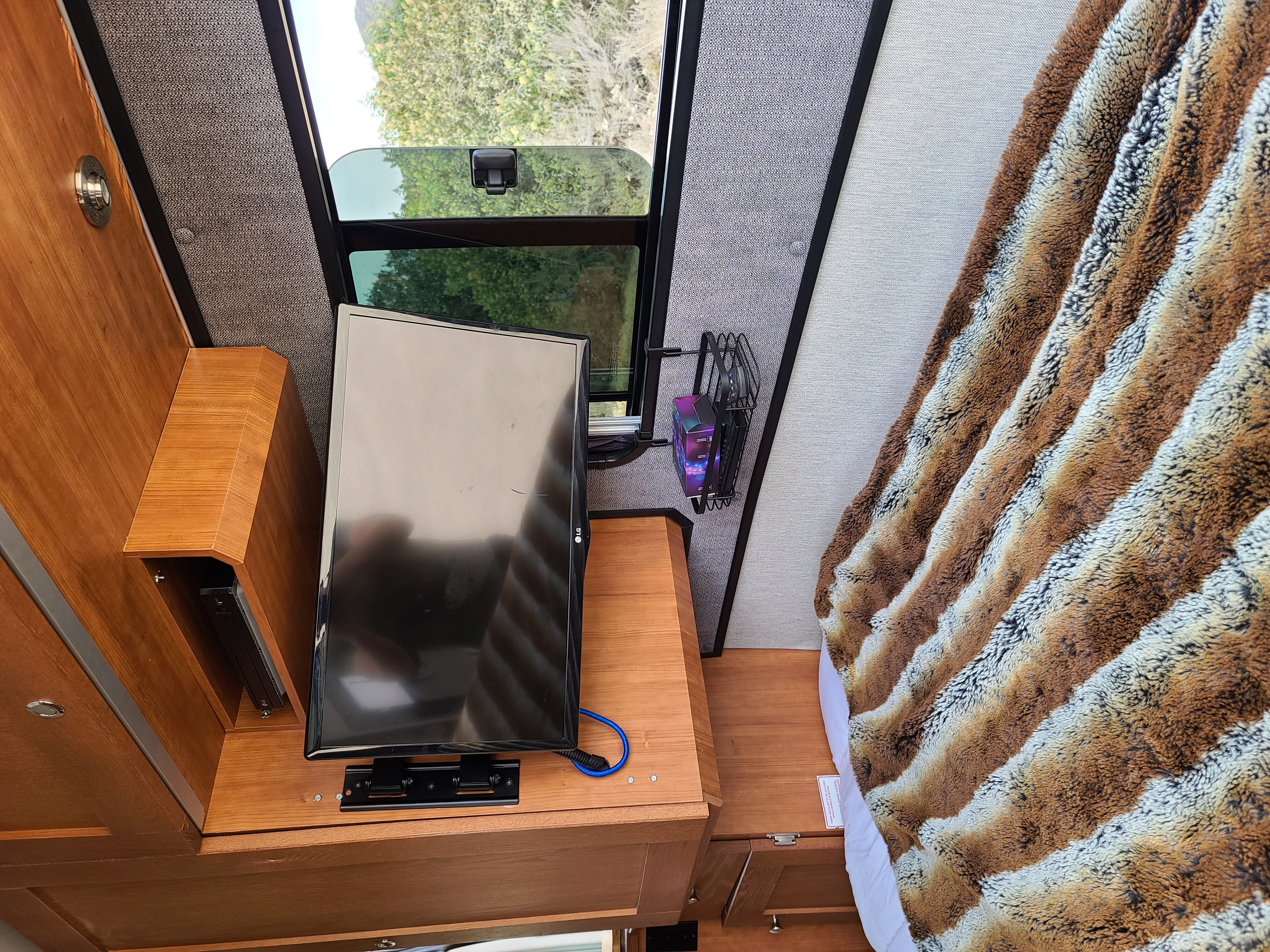 View of an RV rental interior featuring a TV, DVD player, and a bed with a warm, striped animal print blanket.. Roadtrek Roadtrek Class B 2018