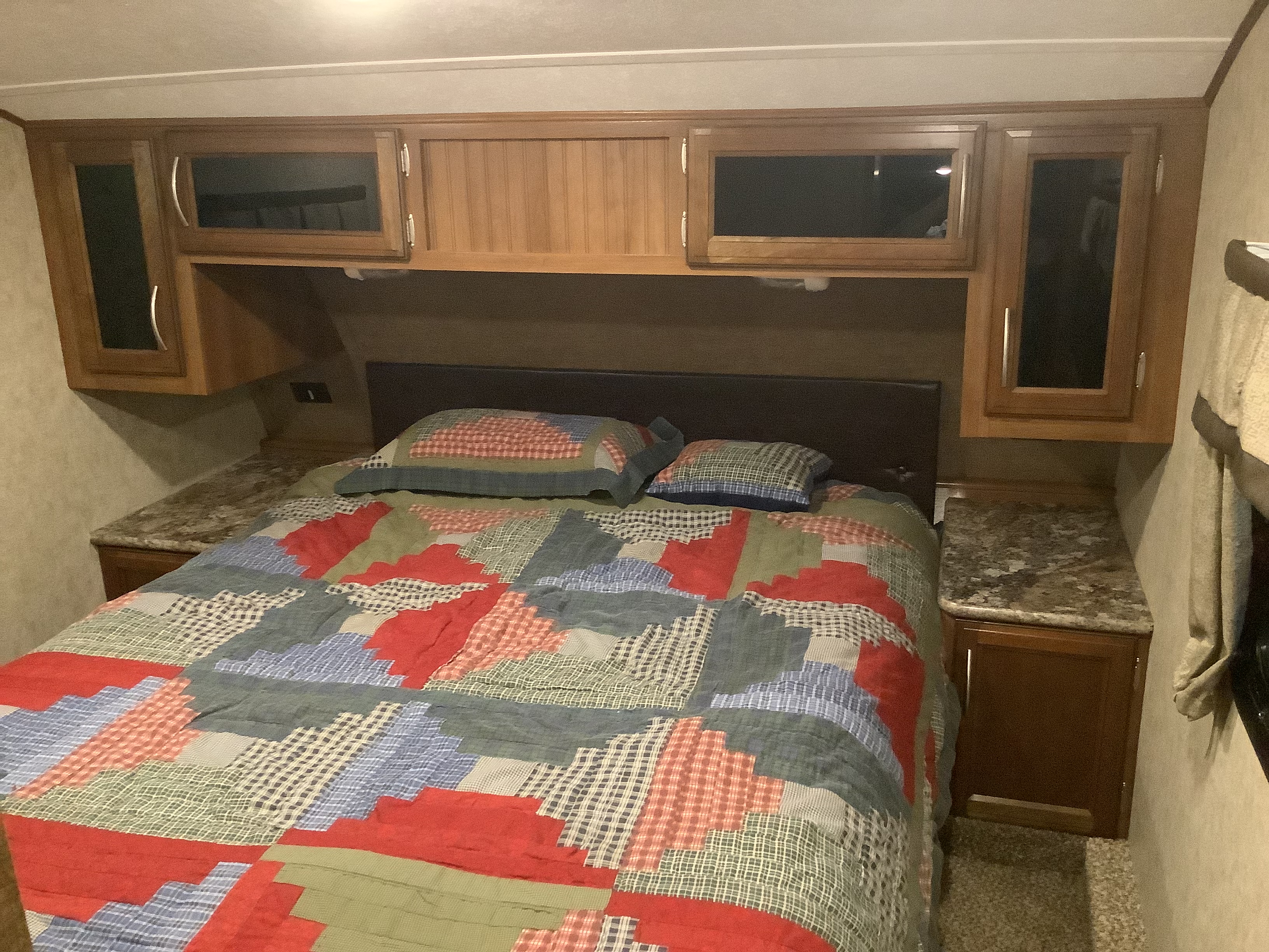 Cozy RV rental bedroom featuring a colorful quilt on the bed, overhead storage cabinets, and compact nightstands.. Prime Time Crusader 2016