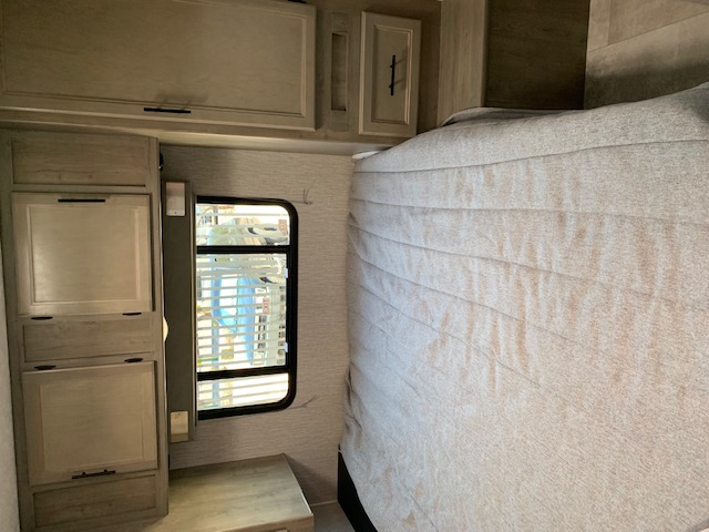 Cozy RV rental bedroom interior: a neatly made bed, light wood cabinets, and a window with blinds offering a glimpse outside.. Coachmen Freelander 2021