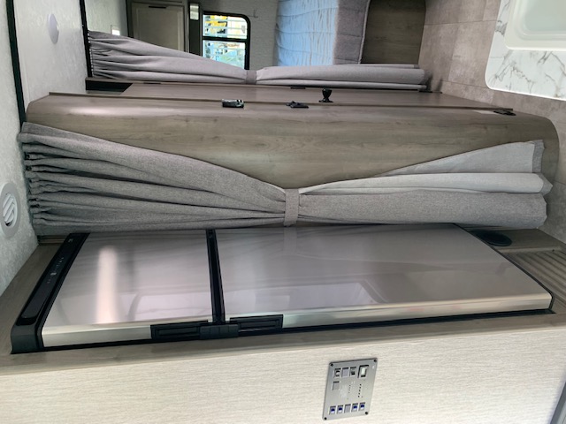 RV rental interior features a bunk bed, tied curtains, a stainless steel RV fridge/cooler, and a control panel below.. Coachmen Freelander 2021