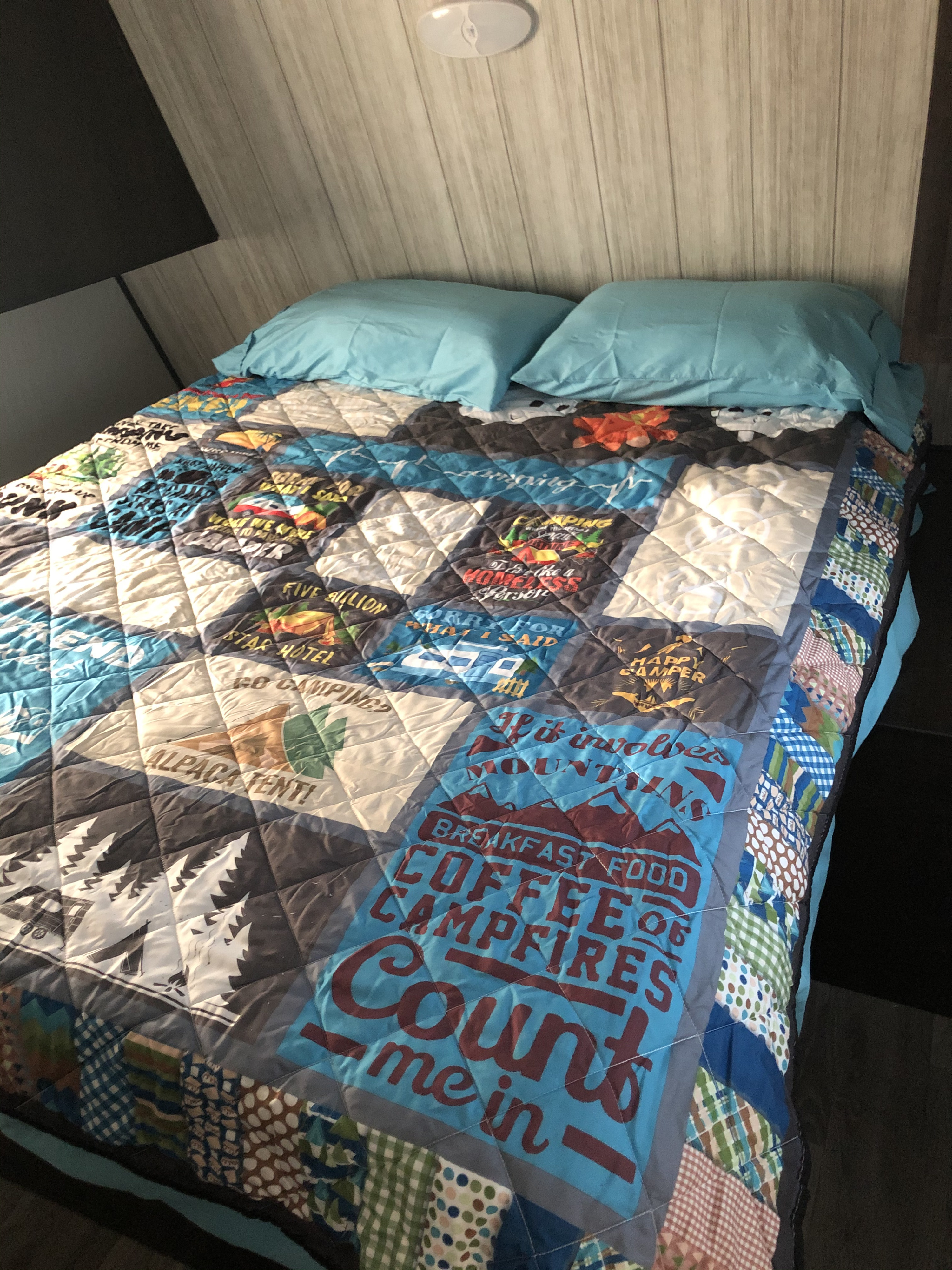 Cozy RV rental bed with a camping-themed quilt and blue pillows, ready for a comfortable stay on your adventure.. Heartland Pioneer 2020