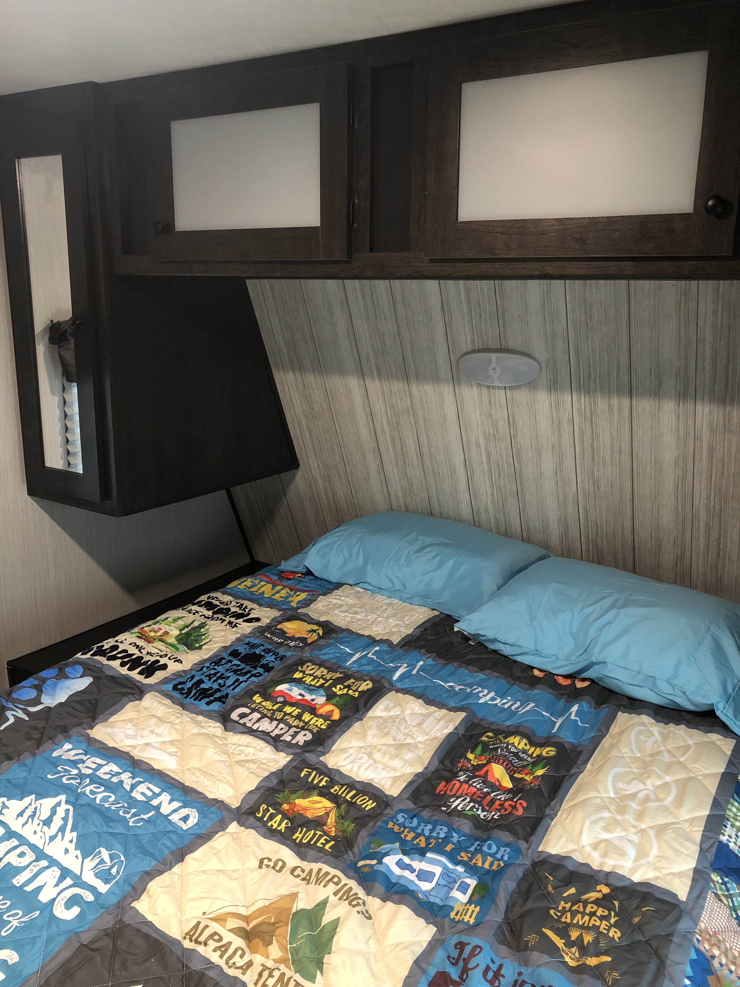 Cozy RV rental bedroom with a fun camping quilt, blue pillows, and overhead storage, ideal for a comfortable trip.. Heartland Pioneer 2020