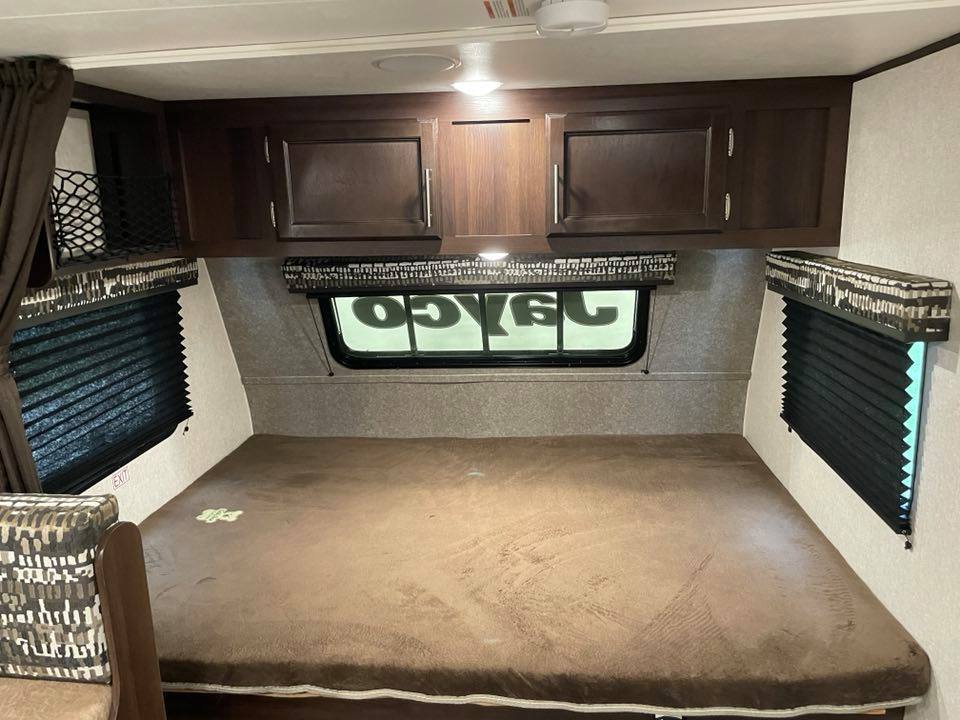 Comfortable RV rental bed, surrounded by dark wood cabinets and windows with blinds.. Jayco Jay Flight 2020