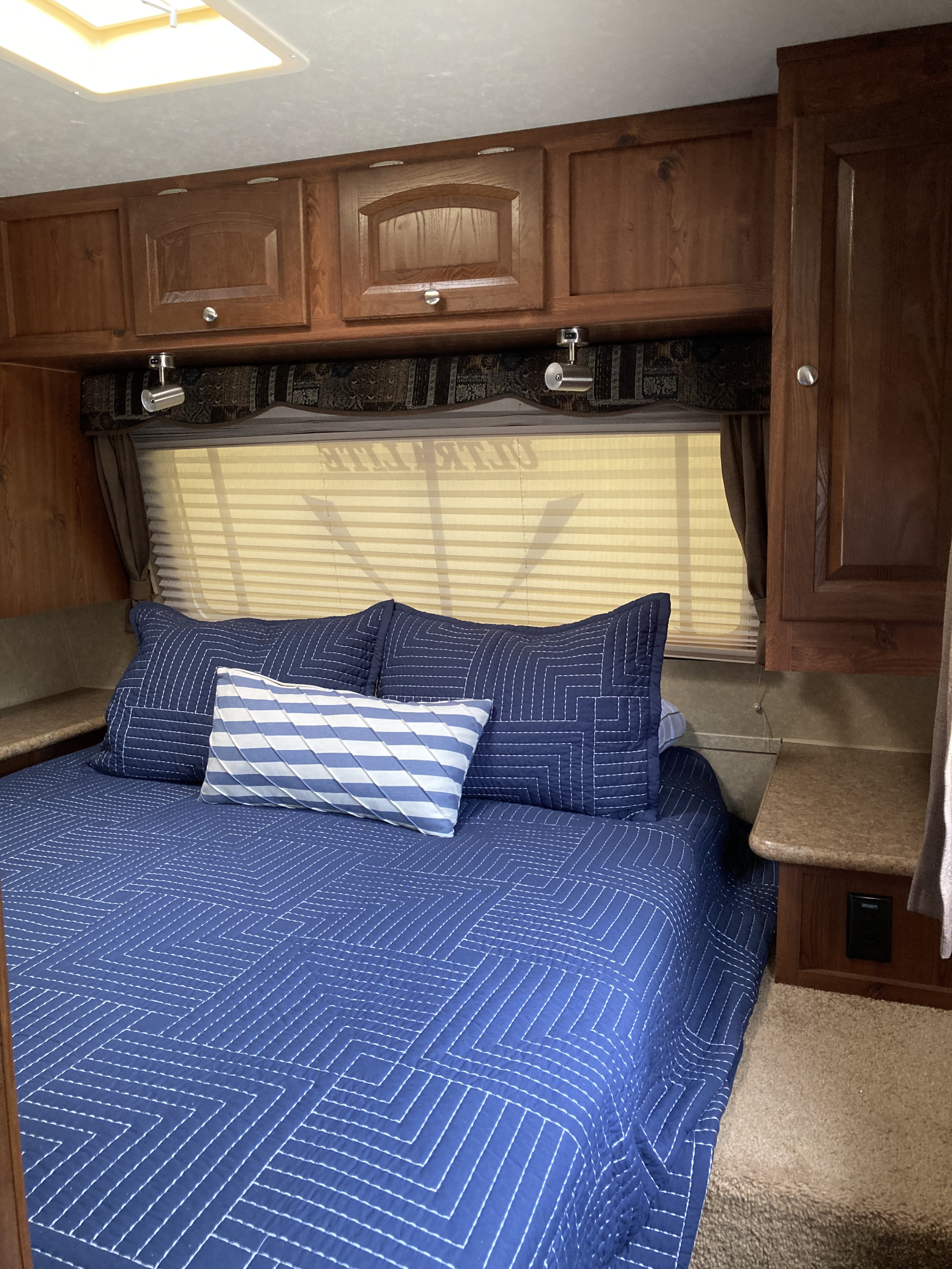 Inside an RV rental: a comfortable bedroom with blue geometric bedding, overhead cabinets, and window blinds.. Forest River Rockwood Ultra Lite 2011