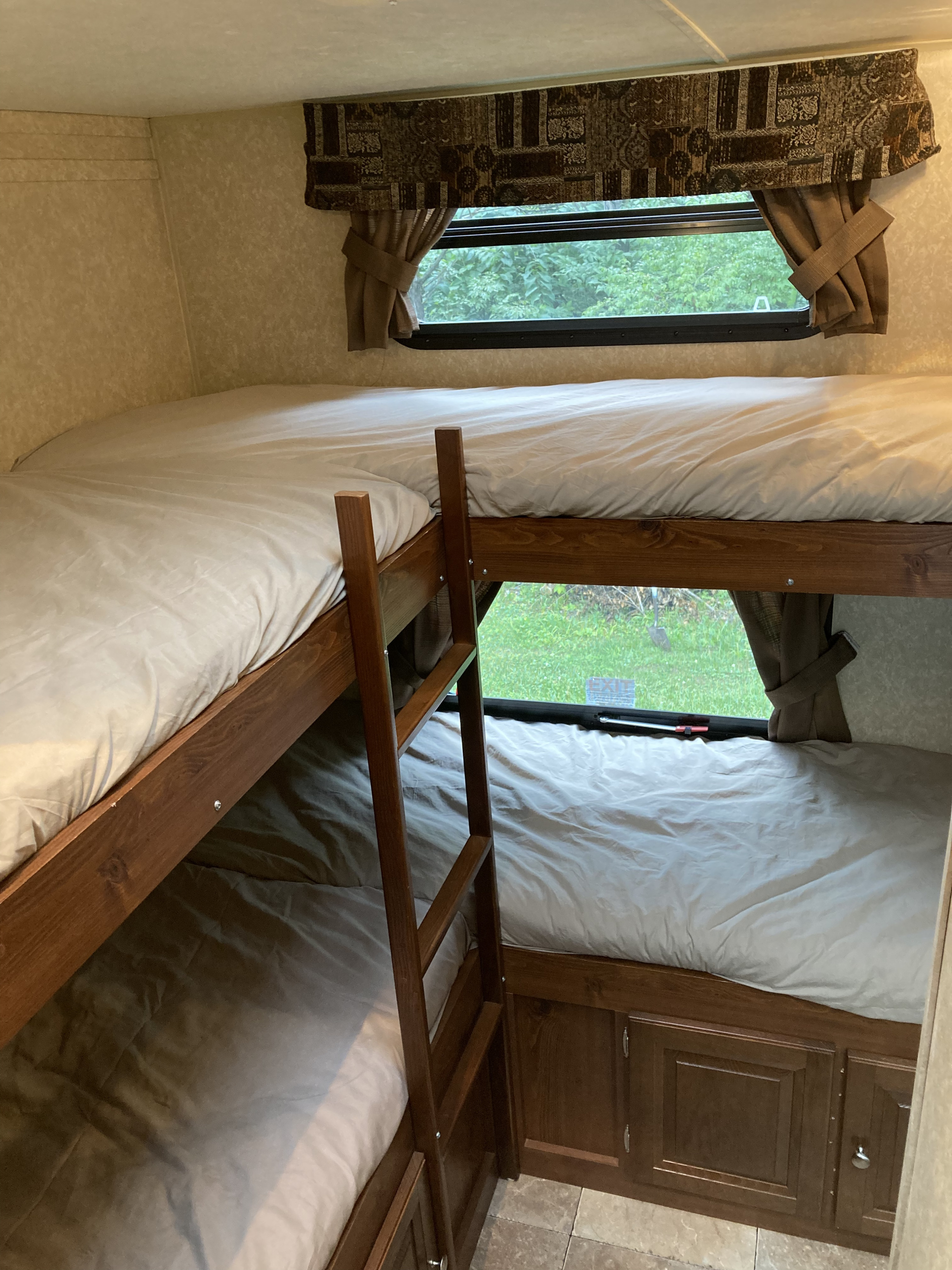 Cozy RV rental bunk beds with a ladder and a window offering a lush nature view. Ideal for family adventures.. Forest River Rockwood Ultra Lite 2011