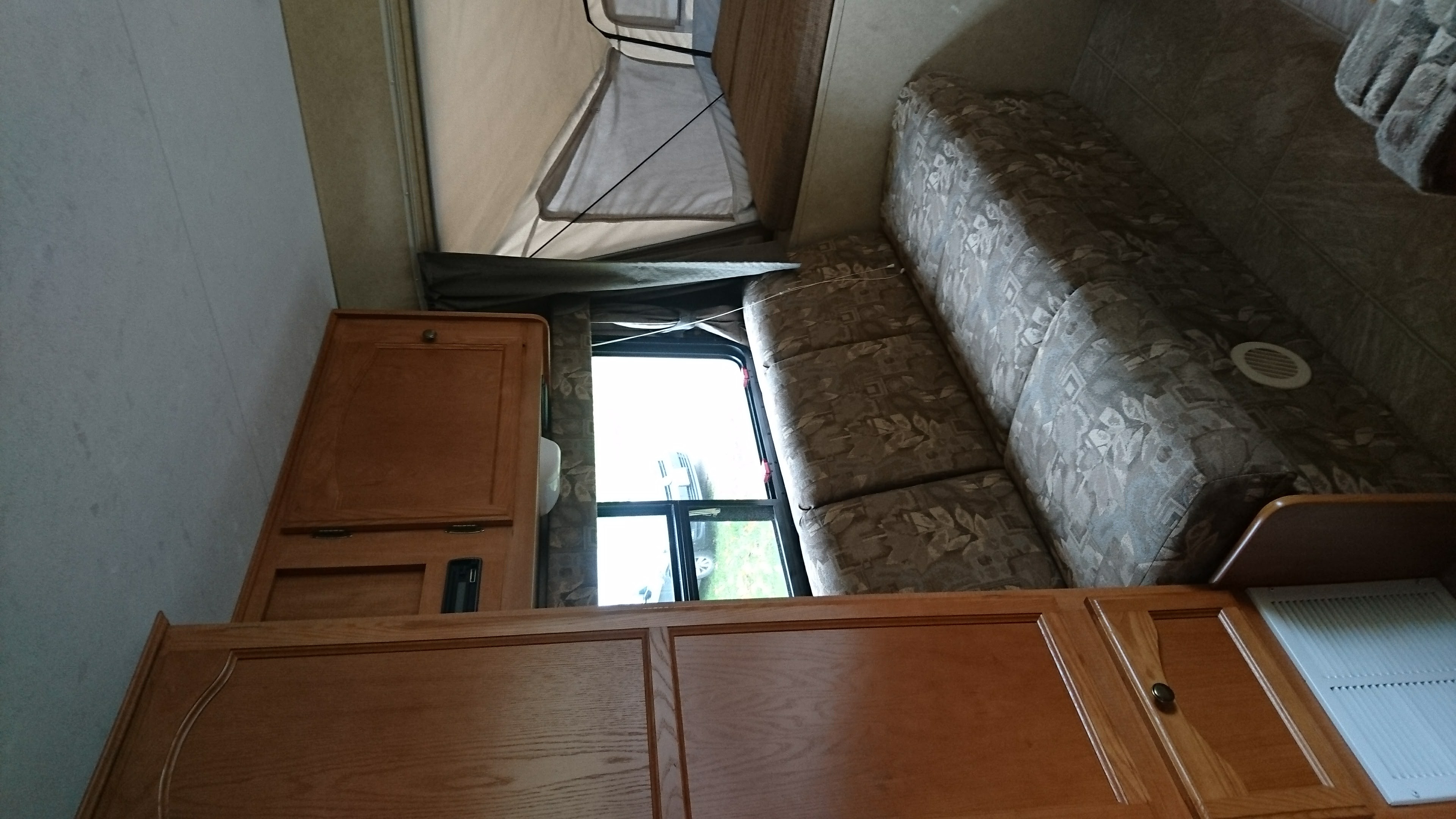 Inside an RV rental: a cozy interior with wooden cabinets, a patterned sofa, and a pop-up bed area.. Starcraft Travel Star 2007