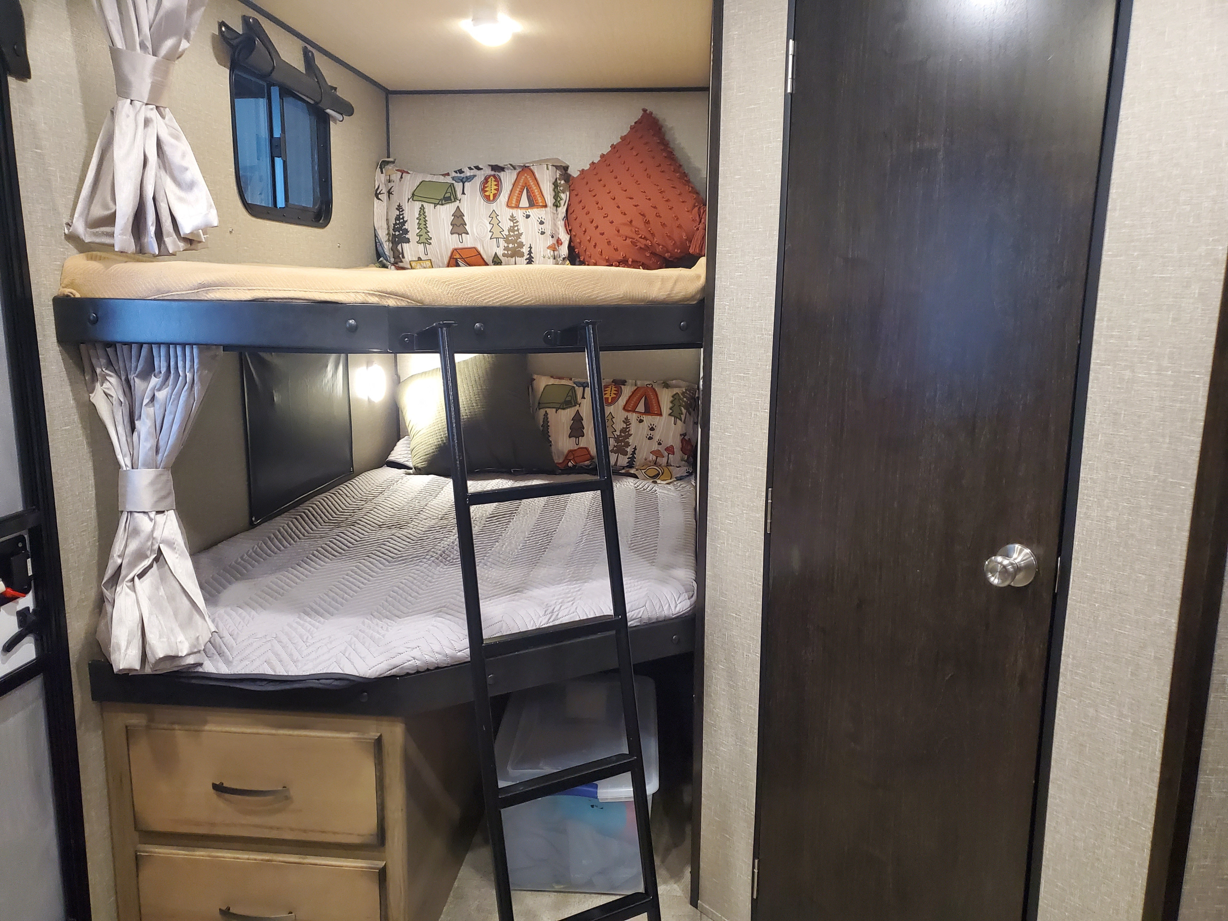 Cozy bunk beds in an RV rental, complete with a ladder, window, and camping-themed decor. The interior includes storage and lights.. Grand Design Transcend 2019