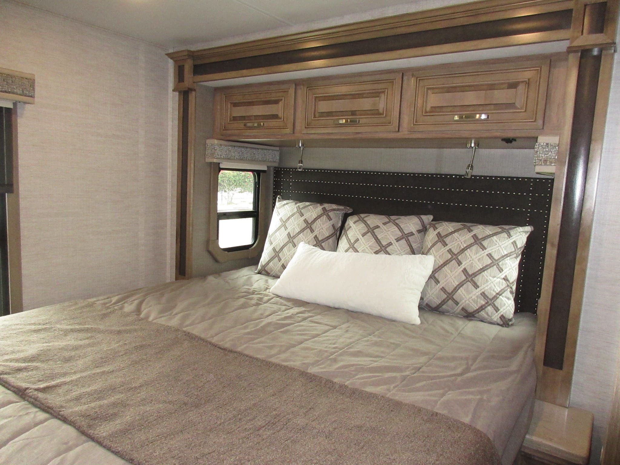 Cozy RV rental bedroom showcasing a comfortable bed, studded headboard, and convenient overhead cabinets for your journey.. Jayco Seneca 2021