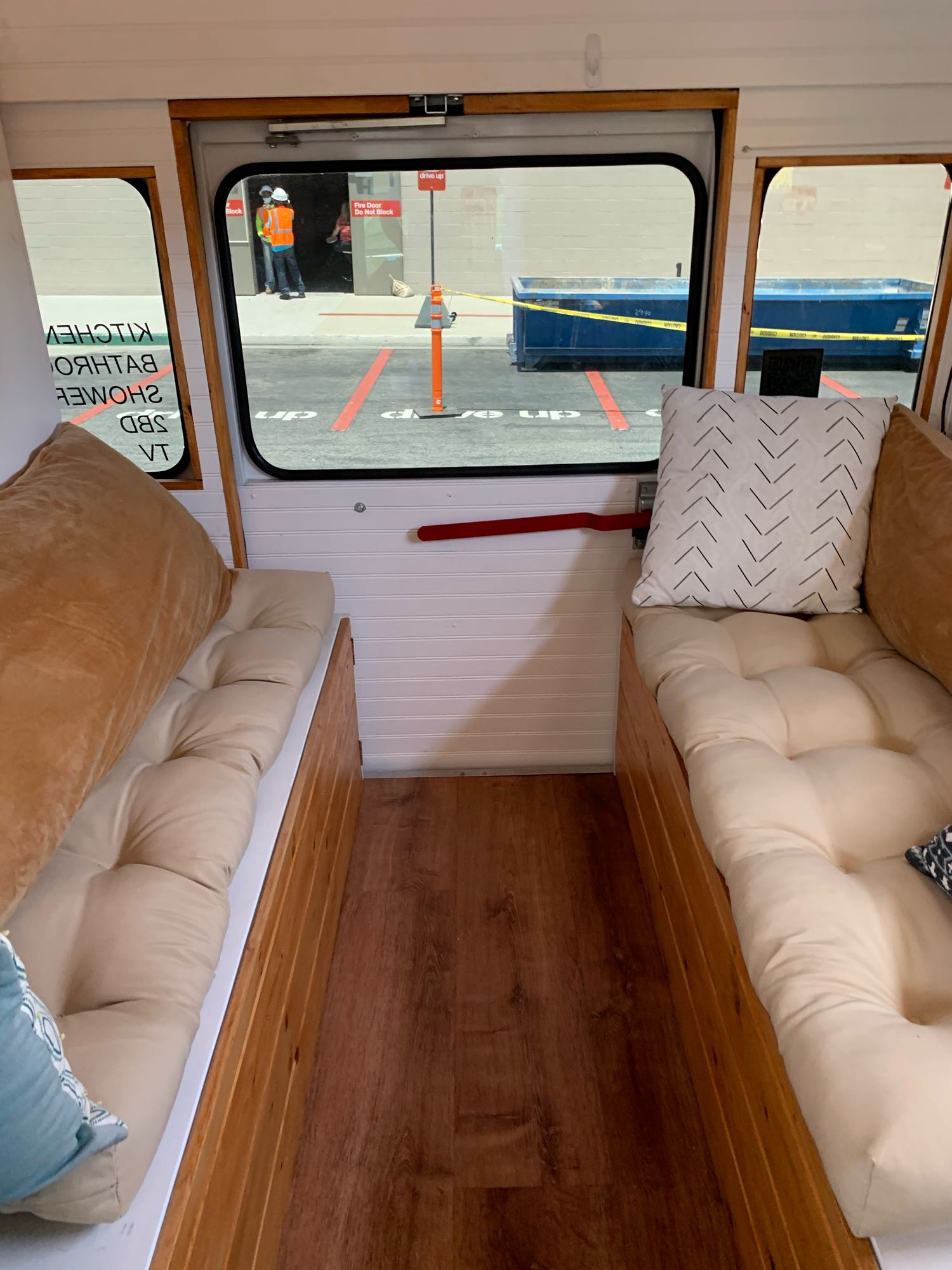 Cozy RV rental interior features two cushioned benches with pillows, wooden floor, and a view of an urban street outside.. Chevrolet Express 2012