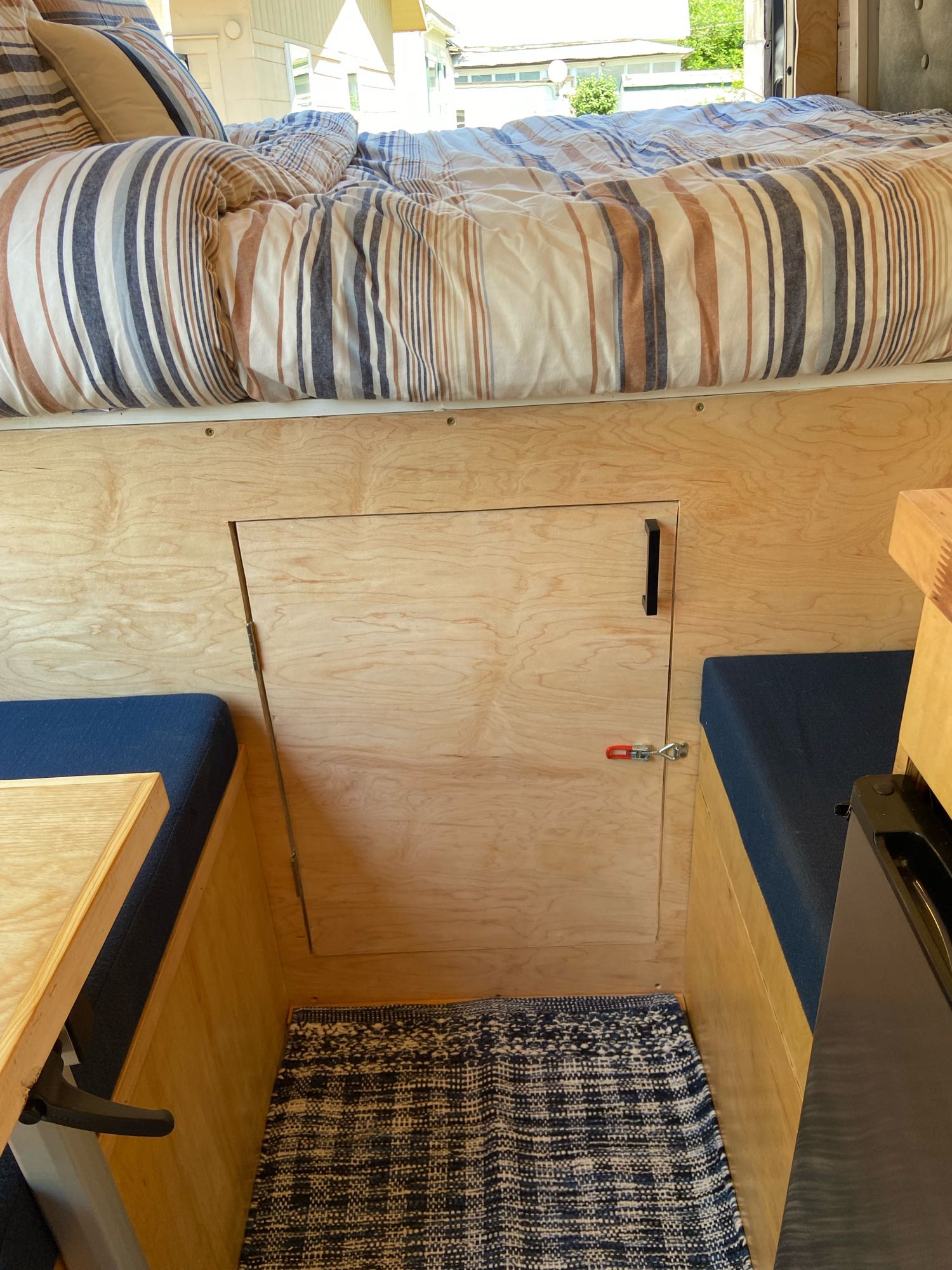 Cozy RV rental interior with striped bed, wood paneling, and a small dinette area with blue cushions.. Freightliner Sprinter 2009