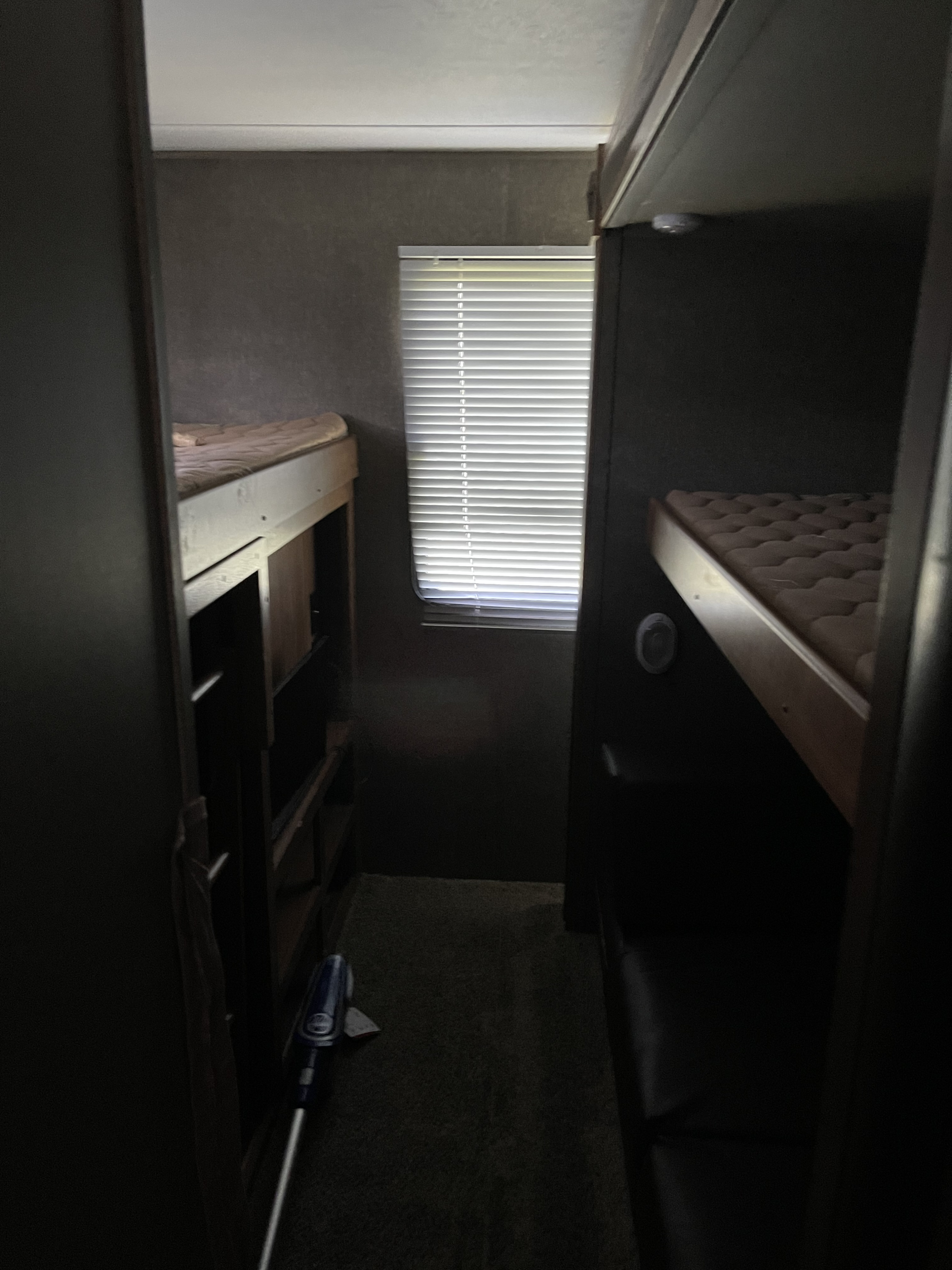 RV rental interior: A narrow aisle flanked by two bunk beds with mattresses. A window with blinds illuminates this compact sleeping area.. Keystone Summerland 2017
