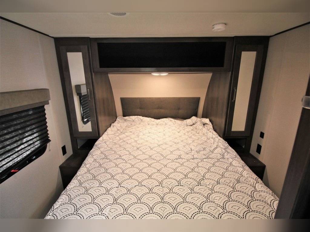 RV rental bedroom with a comfortable bed, dark wood overhead & side storage cabinets, and a window for a cozy stay.. Grand Design Transcend Xplor 2021