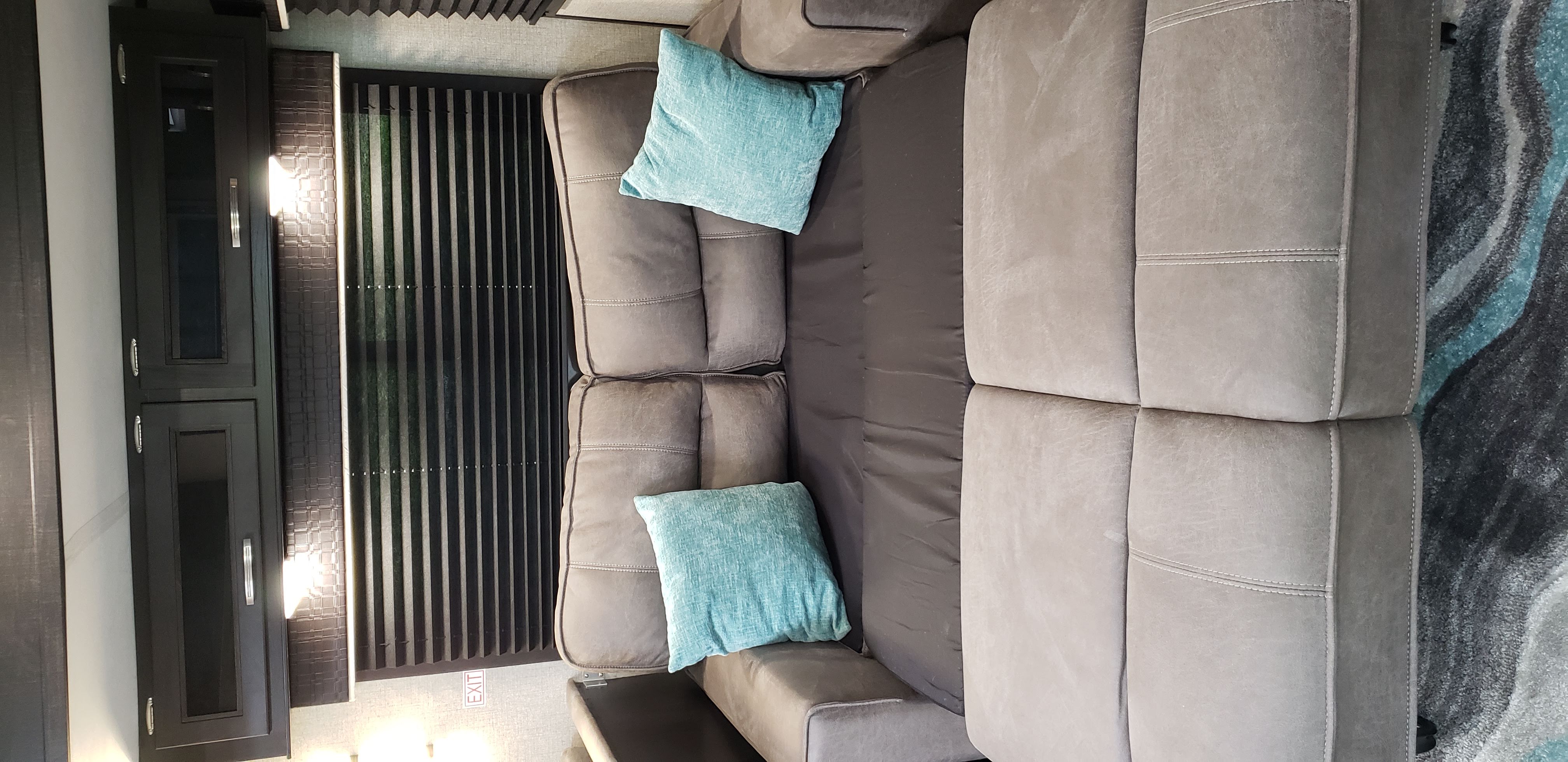 Comfortable RV rental interior with a gray sofa, teal pillows, stylish cabinets, and modern blinds, offering a cozy living area.. Jayco Jay Flight 2021