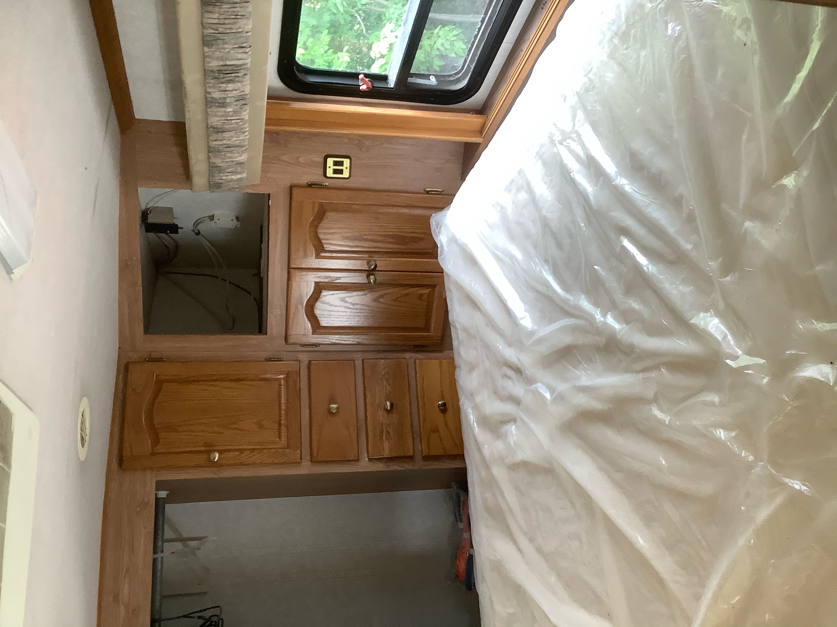 RV rental bedroom interior, featuring wood cabinets, a bed with protective plastic, and an open window.. Tiffin Motorhomes Allegro Bay 2000