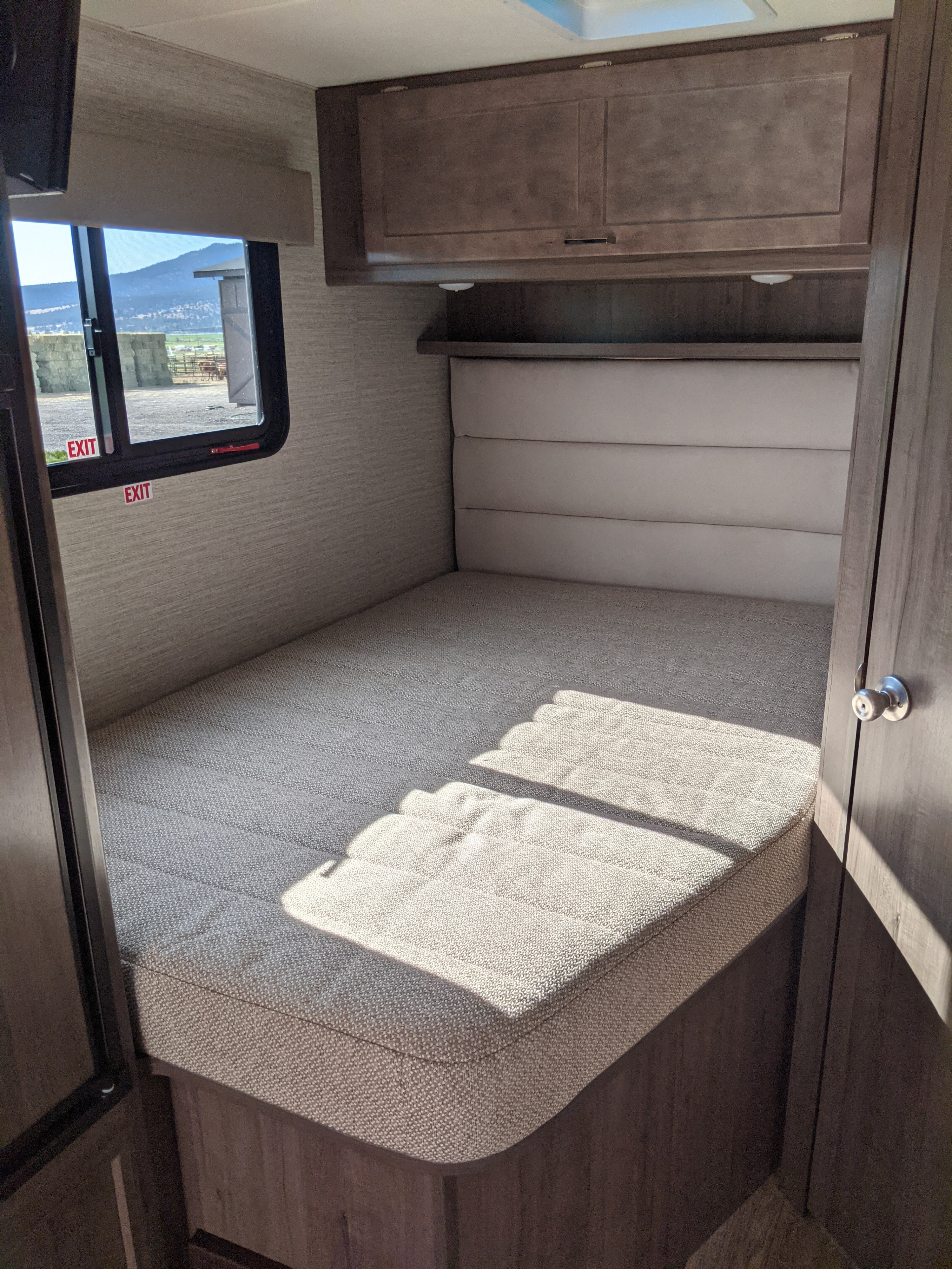 RV rental bedroom: a cozy interior with a comfortable bed, overhead cabinets, and sunlit window overlooking a rural scene.. Winnebago Minnie Winnie 2022